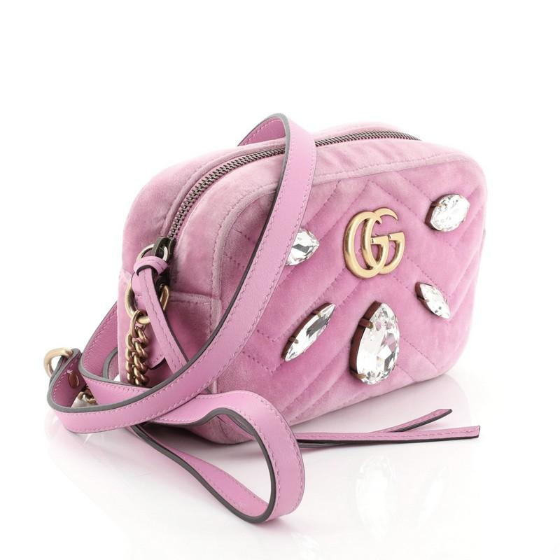 This Gucci GG Marmont Shoulder Bag Crystal Embellished Matelasse Velvet Mini, crafted from pink matelasse velvet, features leather shoulder strap with chain, GG logo and crystal embellishments, and aged gold-tone hardware. Its zip closure opens to a