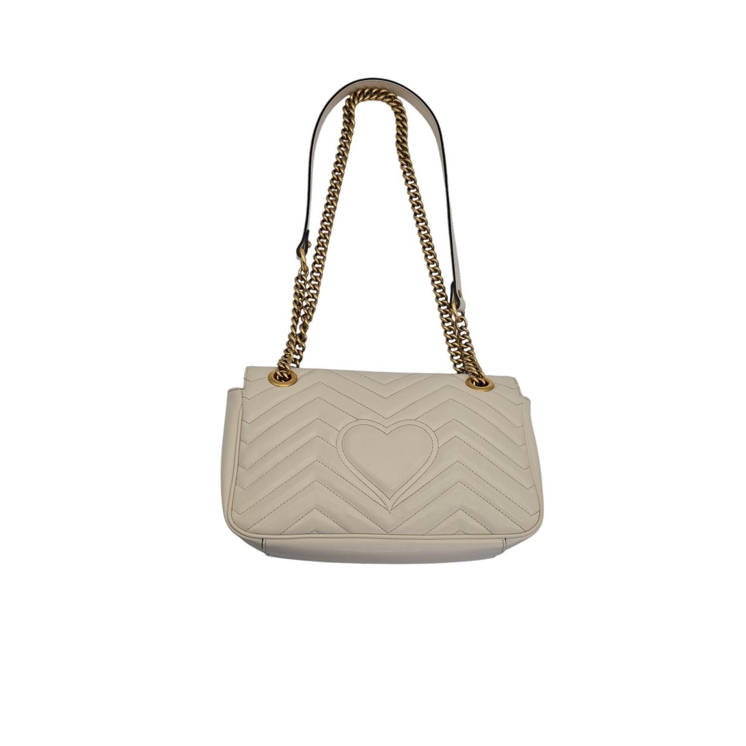 This white Matelassé leather Gucci Small GG Marmont crossbody bag has antiqued gold-tone hardware, single convertible chain-link shoulder strap with leather shoulder guard, peach suede lining, an interior pocket with zip closure and push-lock