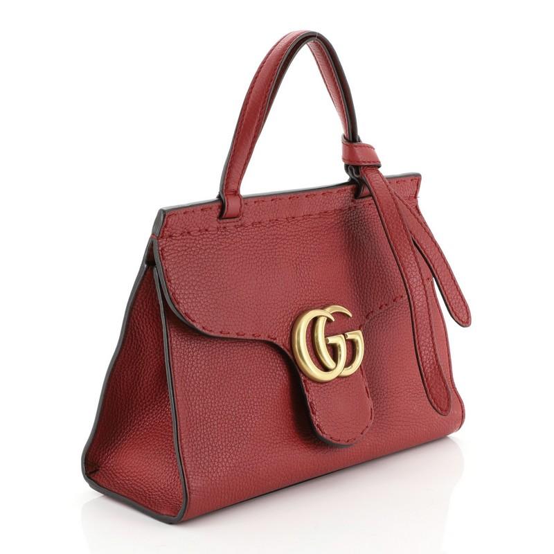 This Gucci GG Marmont Top Handle Bag Leather Mini, crafted from red leather, features a flat leather handle, flap top with GG logo, and gold-tone hardware. Its push-lock closure opens to a neutral fabric interior with slip pocket. 

Estimated Retail