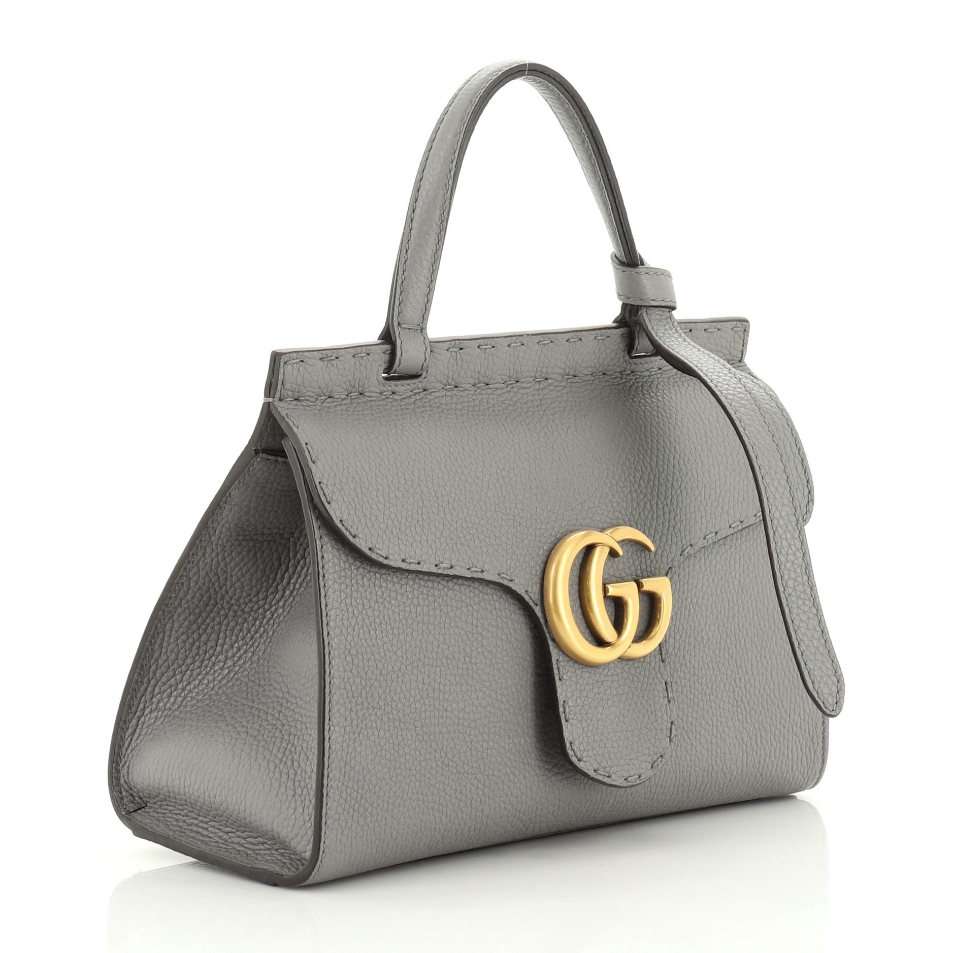 This Gucci GG Marmont Top Handle Bag Leather Mini, crafted from gray leather, features a flat leather handle, flap top with GG logo, and aged gold-tone hardware. Its push-lock closure opens to a neutral fabric interior with slip pocket. 

Condition: