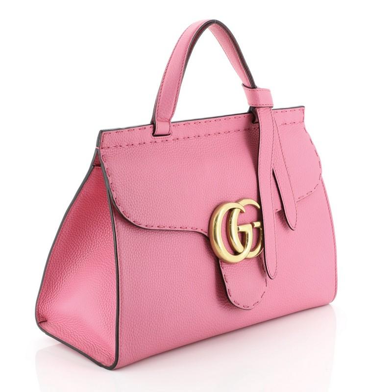 This Gucci GG Marmont Top Handle Bag Leather Small, crafted from pink leather, features flat top handle with knot on one end, flap with GG logo, stitching detail, and aged gold-tone hardware. Its push-lock closure opens to a neutral fabric interior