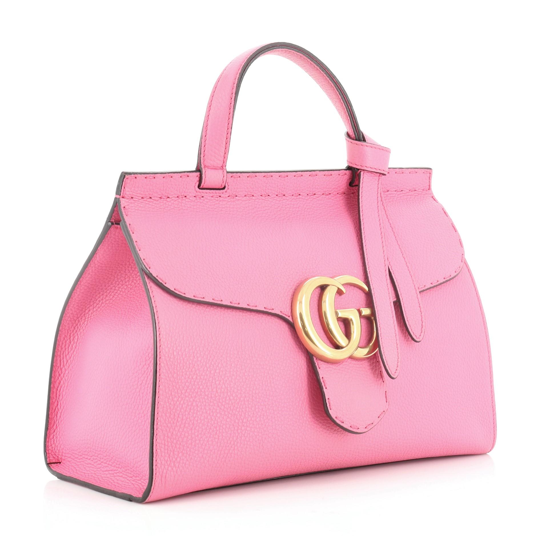 This Gucci GG Marmont Top Handle Bag Leather Small, crafted from pink leather, features a flat leather handle, flap top with GG logo, and aged gold-tone hardware. Its push-lock closure opens to a neutral fabric interior with zip and slip pockets.