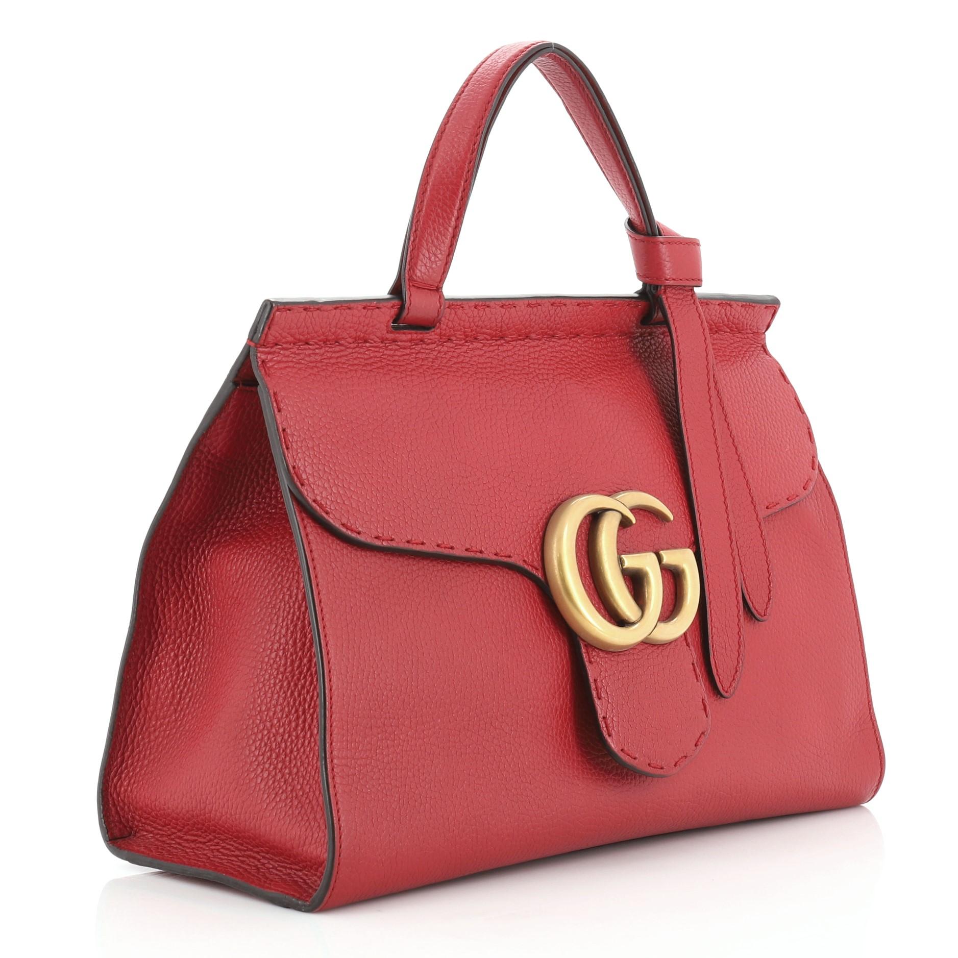 This Gucci GG Marmont Top Handle Bag Leather Small, crafted from red leather, features a flat leather handle, flap top with GG logo, and aged gold-tone hardware. Its push-lock closure opens to a neutral fabric interior with zip and slip pockets.