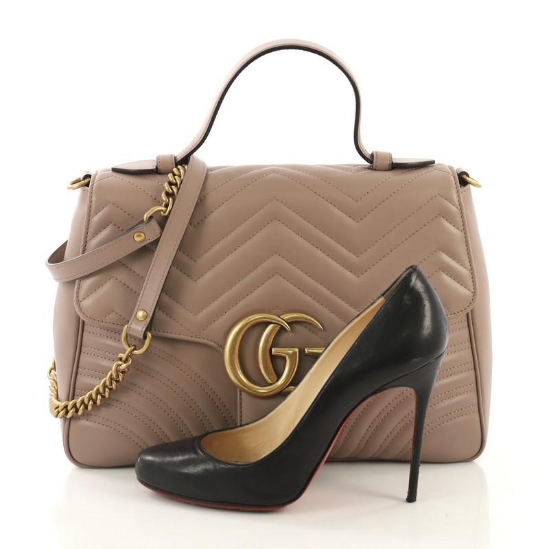 This Gucci GG Marmont Top Handle Flap Bag Matelasse Leather Medium, crafted from mauve matelasse leather, features a flat leather handle, flap top with GG logo, and aged gold-tone hardware. Its push-lock closure underneath the flap opens to a nude