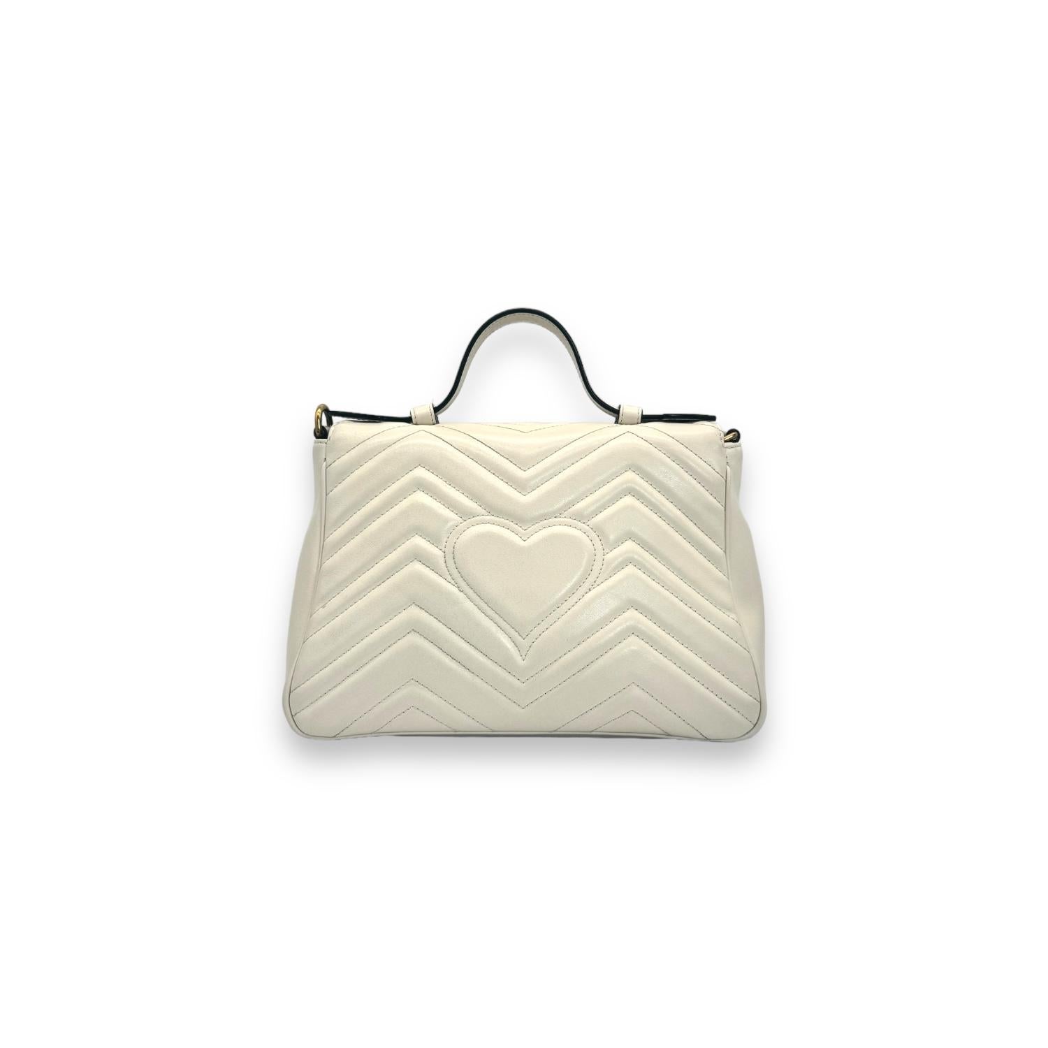 Experience luxury and style with the Gucci GG Marmont Top Handle Small Crossbody Bag. Made in Italy with white matelassé chevron leather and antique gold-tone hardware, this versatile bag exudes elegance. It features a push snap closure at the