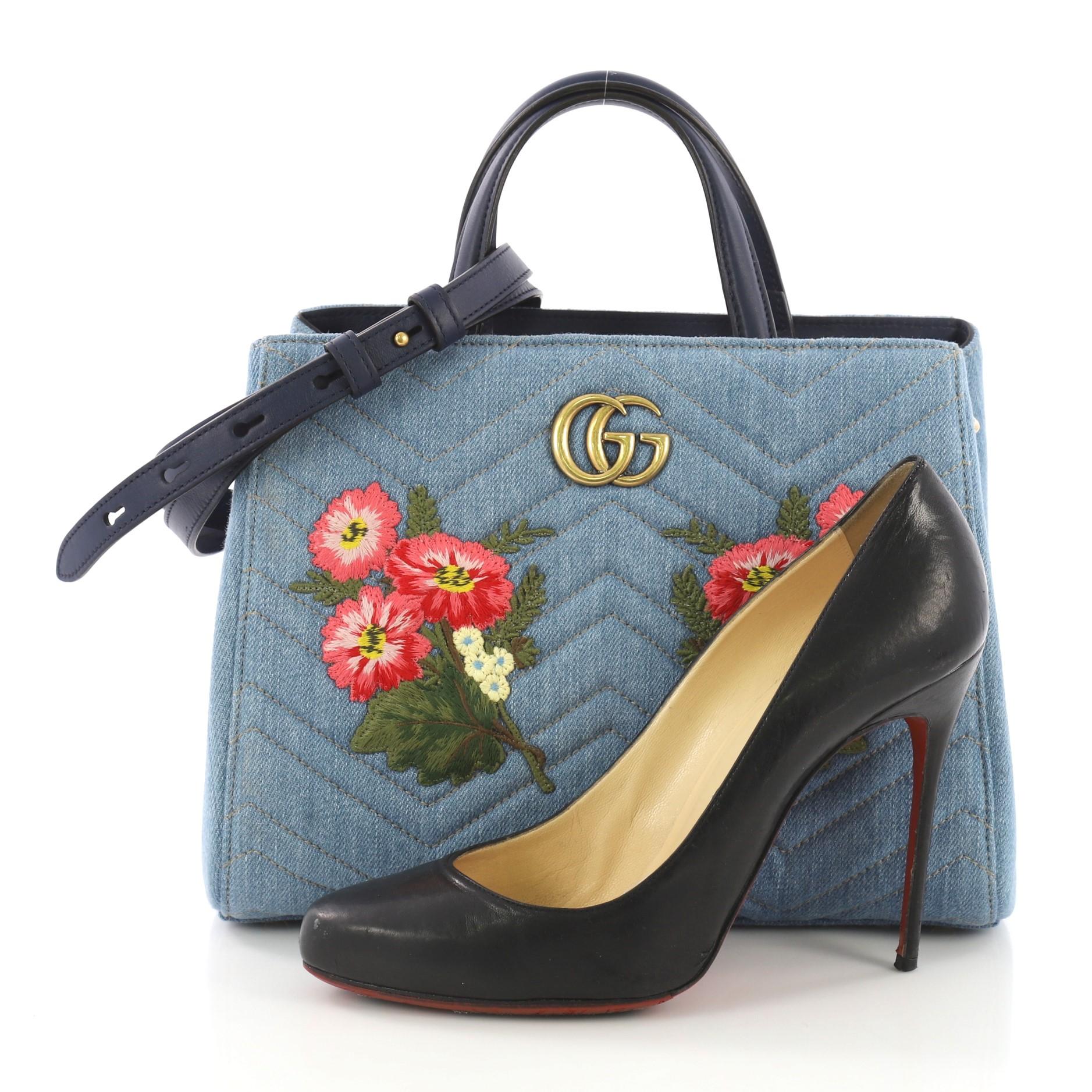This Gucci GG Marmont Tote Embroidered Matelasse Denim Small, crafted from blue embroidered matelasse denim, features dual top leather handles, interlocking GG logo, floral embroidery details, and aged gold-tone hardware. Its magnetic snap closure