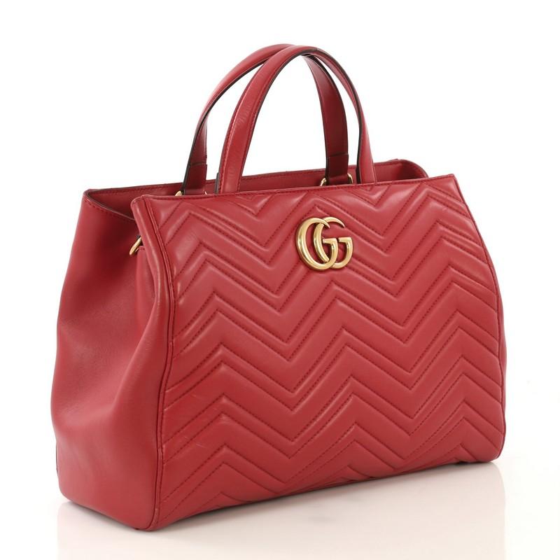 This Gucci GG Marmont Tote Matelasse Leather Medium, crafted from red matelasse leather, features dual flat handles, metal GG logo, GG stitching detail at the back, protective base studs and aged gold-tone hardware. Its magnetic snap closure opens