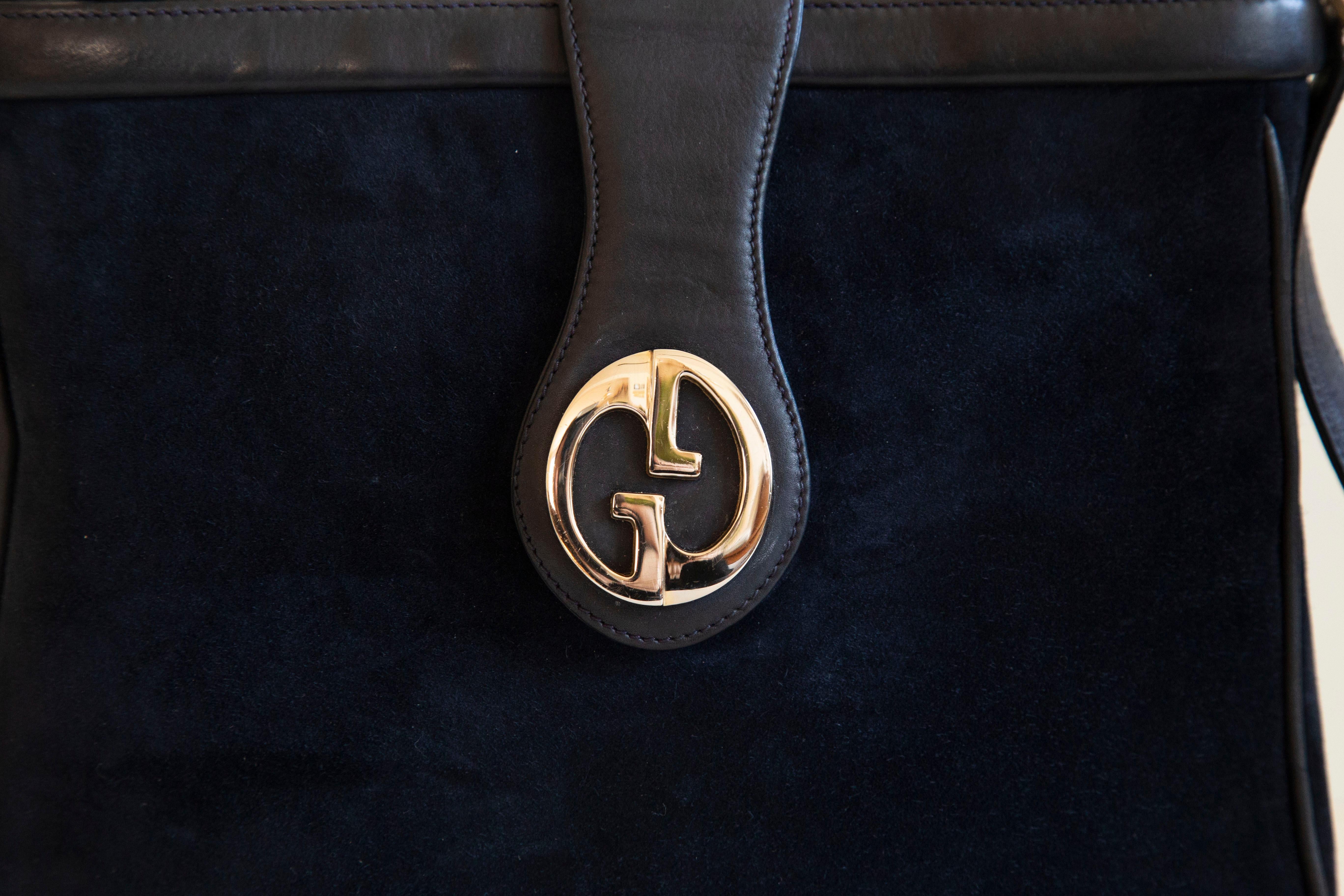A vintage Gucci GG shoulder bag ca. 1970s, Italy. This bag features a dark blue suede exterior, silver tone GG hardware, and soft dark blue leather trim. The interior is lined with dark blue leather and there are two side pockets with a zipper. The