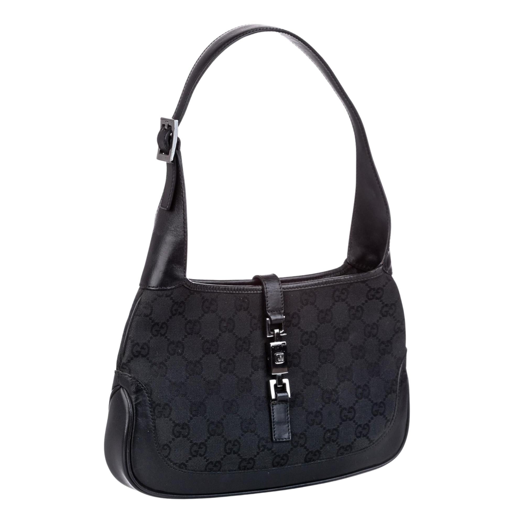 This Gucci Jackie bag is made of black monogram GG canvas. The bag features black leather finishes including the looping flat leather shoulder strap, base and pipping. The bag is finished with a crossover strap with a silver piston lock that opens