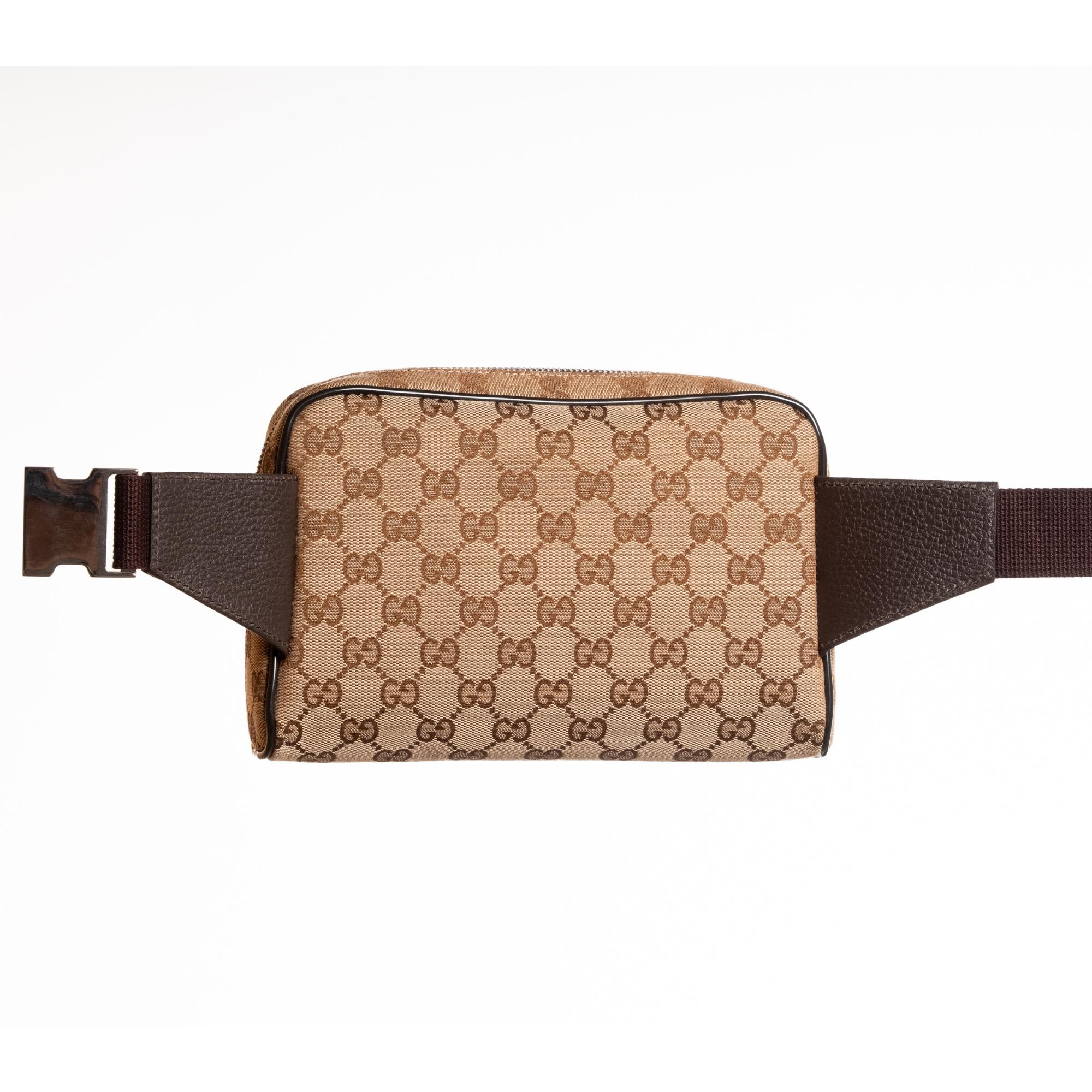 This classic Gucci belt bag in ebony/beige monogram canvas is made of canvas with canvas with leather finishes. The bag features the classic monogram print, leather pipping in contrasting brown, top zip closure, a woven fabric bet with buckle and an