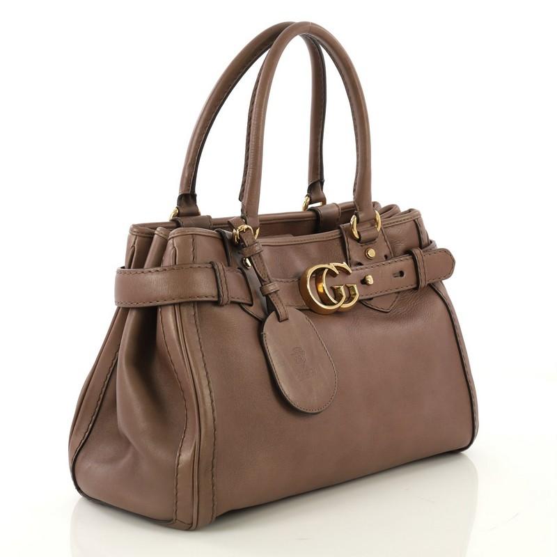 This Gucci GG Running Tote Leather Medium, crafted in taupe leather, features dual rolled leather top handles, a top belt with loops with a gold Gucci interlocking GG buckle and gold-tone hardware. Its magnetic snap button closure opens to an beige