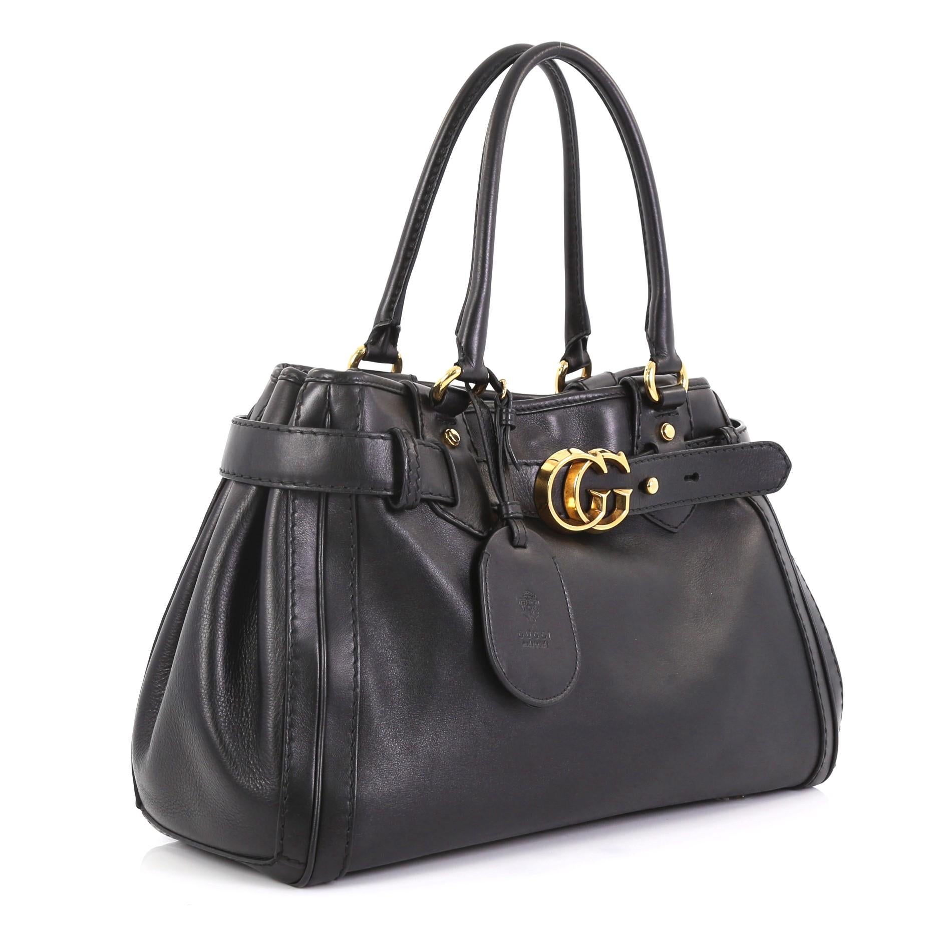 This Gucci GG Running Tote Leather Medium, crafted in black leather, features dual rolled leather top handles, top belt with loops and interlocking GG buckle, protective base studs, and gold-tone hardware. Its magnetic snap button closure opens to a