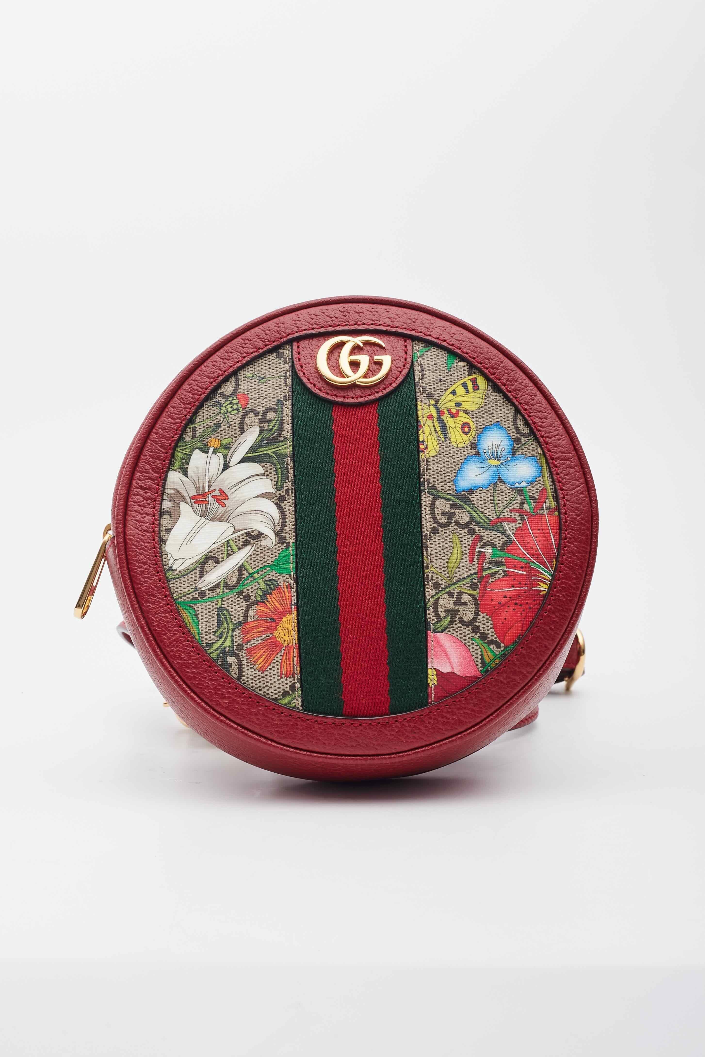 Ce mini sac à dos Gucci présente une toile enduite à monogramme GG, une superposition d'imprimés flore, des ferrures aux tons dorés et une structure ronde. Le sac est doté d'une toile sur le devant et d'une bordure en cuir rouge. La fermeture à