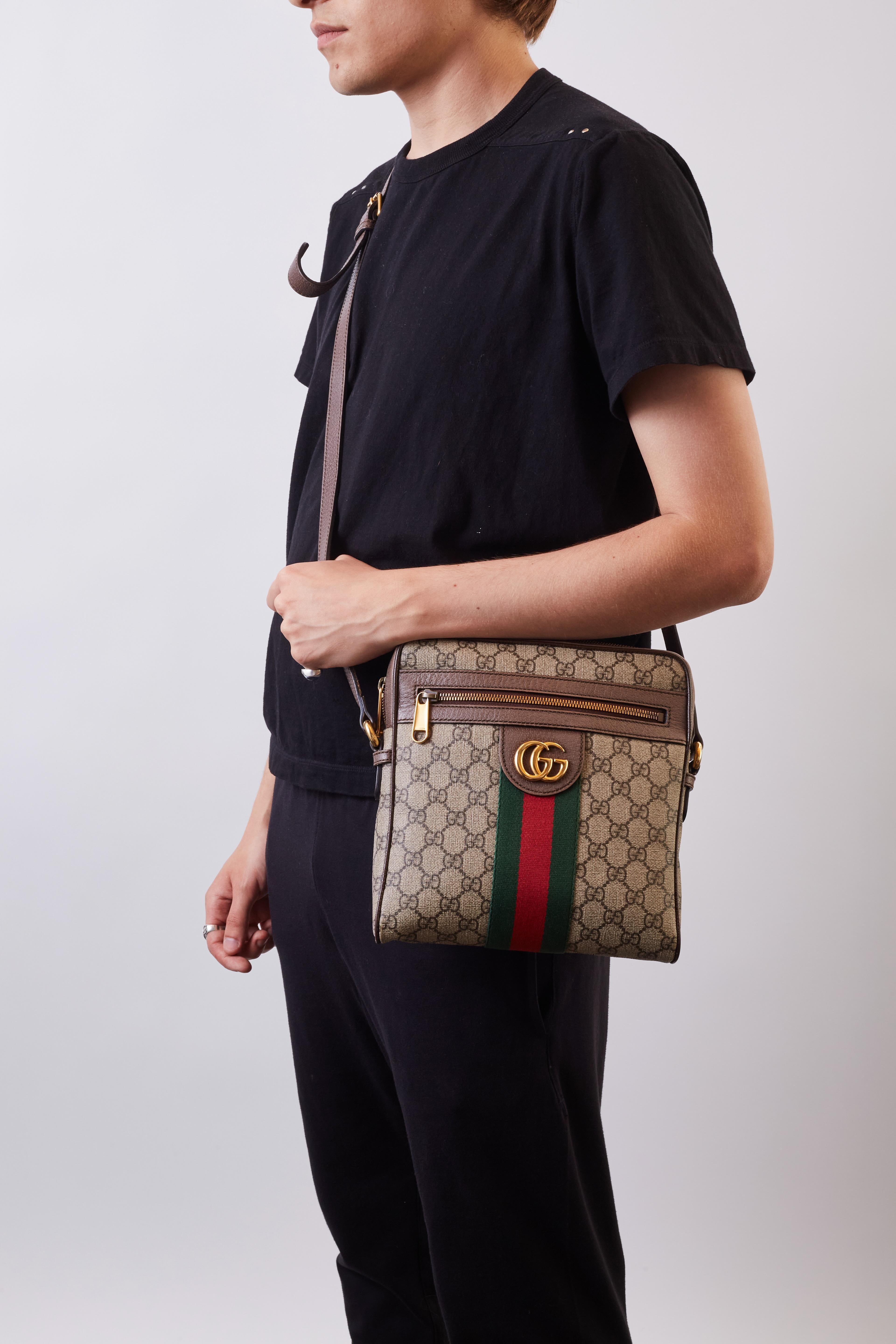 This shoulder bag is constructed of Gucci GG supreme monogram on coated canvas, with brown leather trim and an adjustable shoulder strap. The bag features a front zipper pocket embellished with an aged gold interlocking GG logo, and red and green