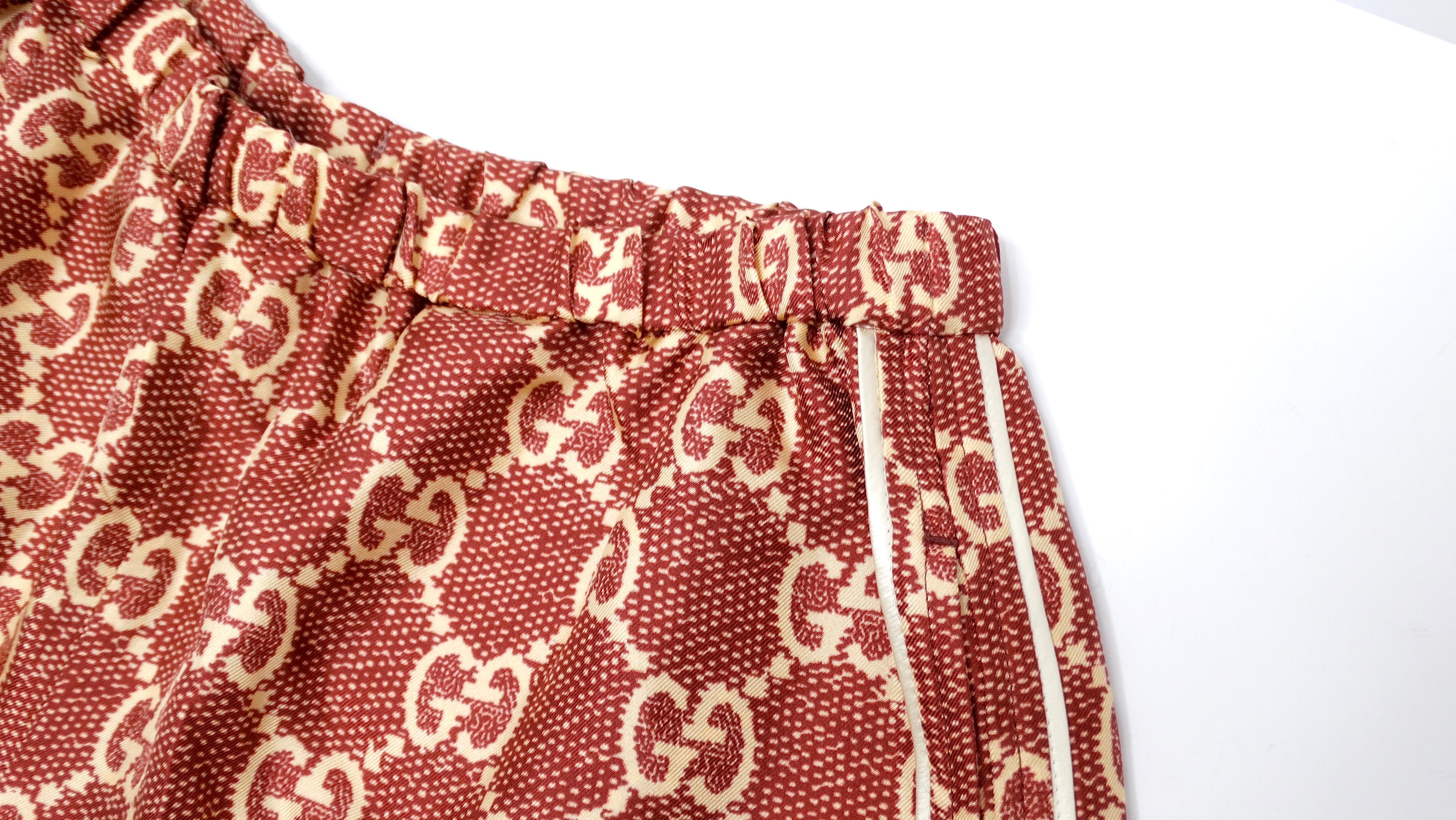 Experience luxury in motion with the Gucci GG Supreme Silk Burgundy Track Shorts. Crafted in Italy from 100% silk, these shorts offer an opulent twist on athletic wear. The rich burgundy hue is elegantly complemented by cream silk track stripes
