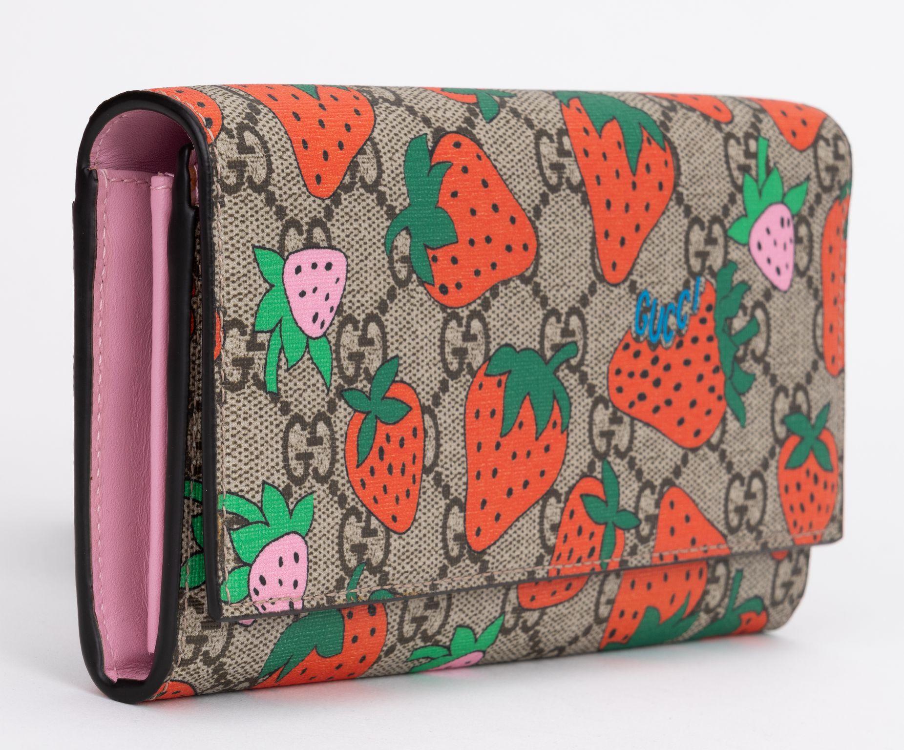 This is an authentic GUCCI GG Supreme Monogram Strawberry Flap Wallet in Light Pink. This stylish wallet is crafted of Gucci GG Supreme monogram coated canvas, with a red and pink strawberry print overlay. The crossover flap opens to a partitioned