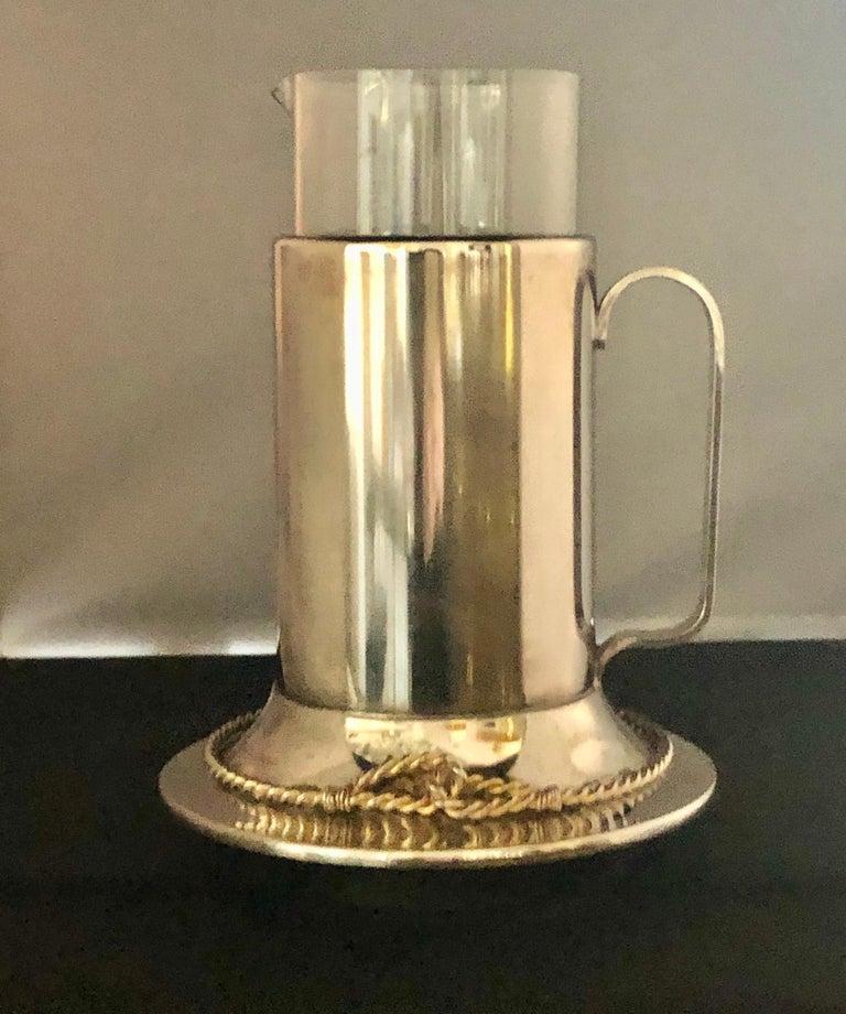 Offered is a signed Gucci Mid-Century Modern or late 20th Century nautical themed glass encased in silver and gold plate vintage martini pitcher with matching French twist in gold and silver elongated stirring spoon.  The glass insert pitcher can be