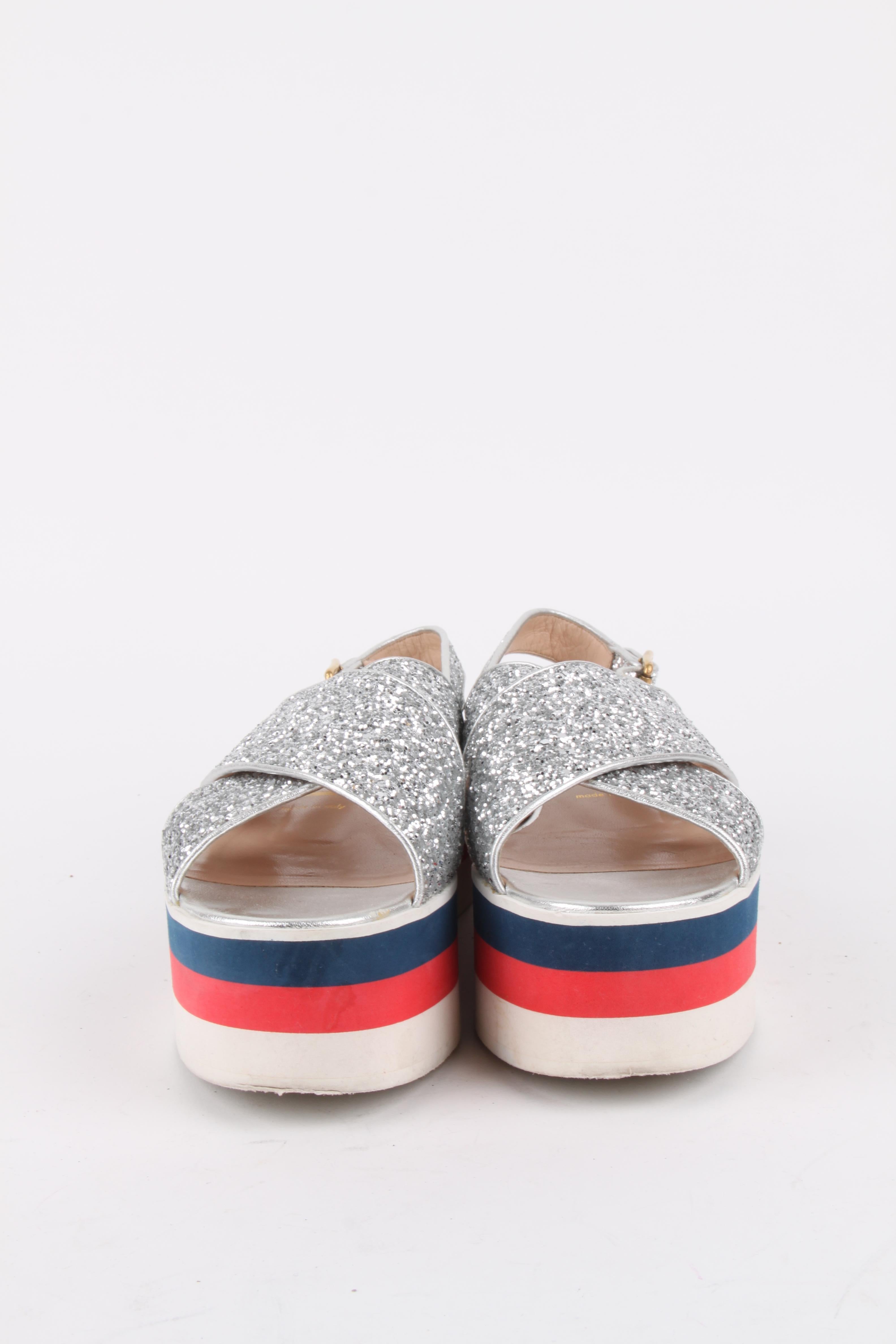Gucci Glitter Crossover Patform Sandals

Silver glitter with metallic silver leather trim
Red, blue and white platform
Crossover front
Adjustable ankle strap closure
Size: 38,5.

Meaurements: Heel : 5cm / 2 inch  / In-sole: 25 cm / 9,8 inch.