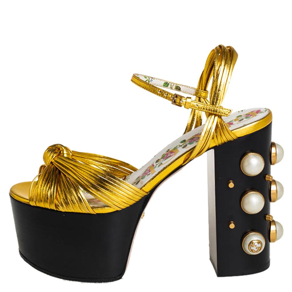Beauty radiates from these sandals from Gucci! Crafted from gold leather, these sandals have knotted vamp straps, ankle straps with buckle fastening, and 13 cm high block heels embellished with studs and faux pearls.

