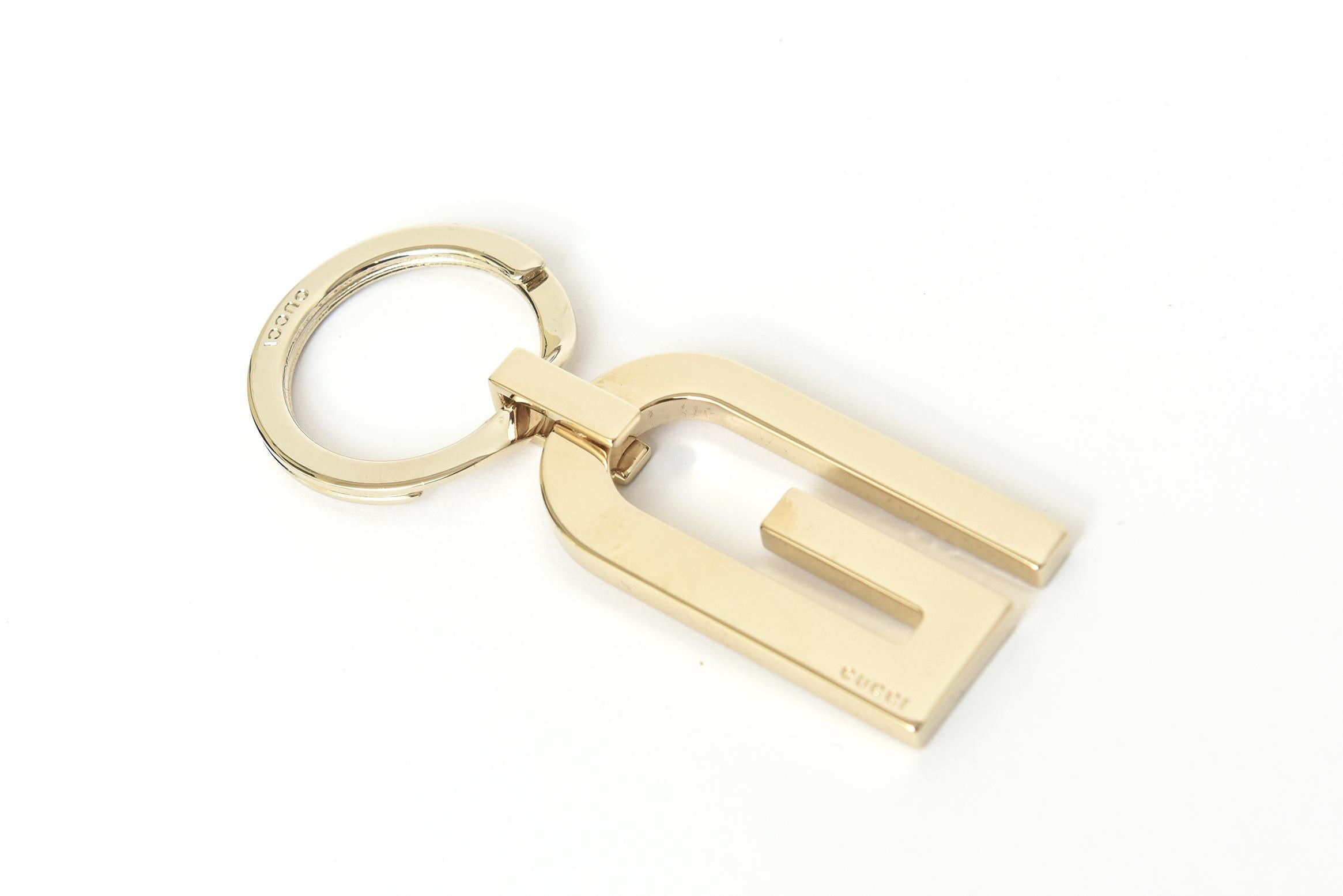 This vintage gold plated Gucci mens key chain can also be unsex. It has the Gucci marked on the bottom right hand side of the G with a small bar connecting to the ring. It was never used and has its original Gucci flap case in black with brown GG's.