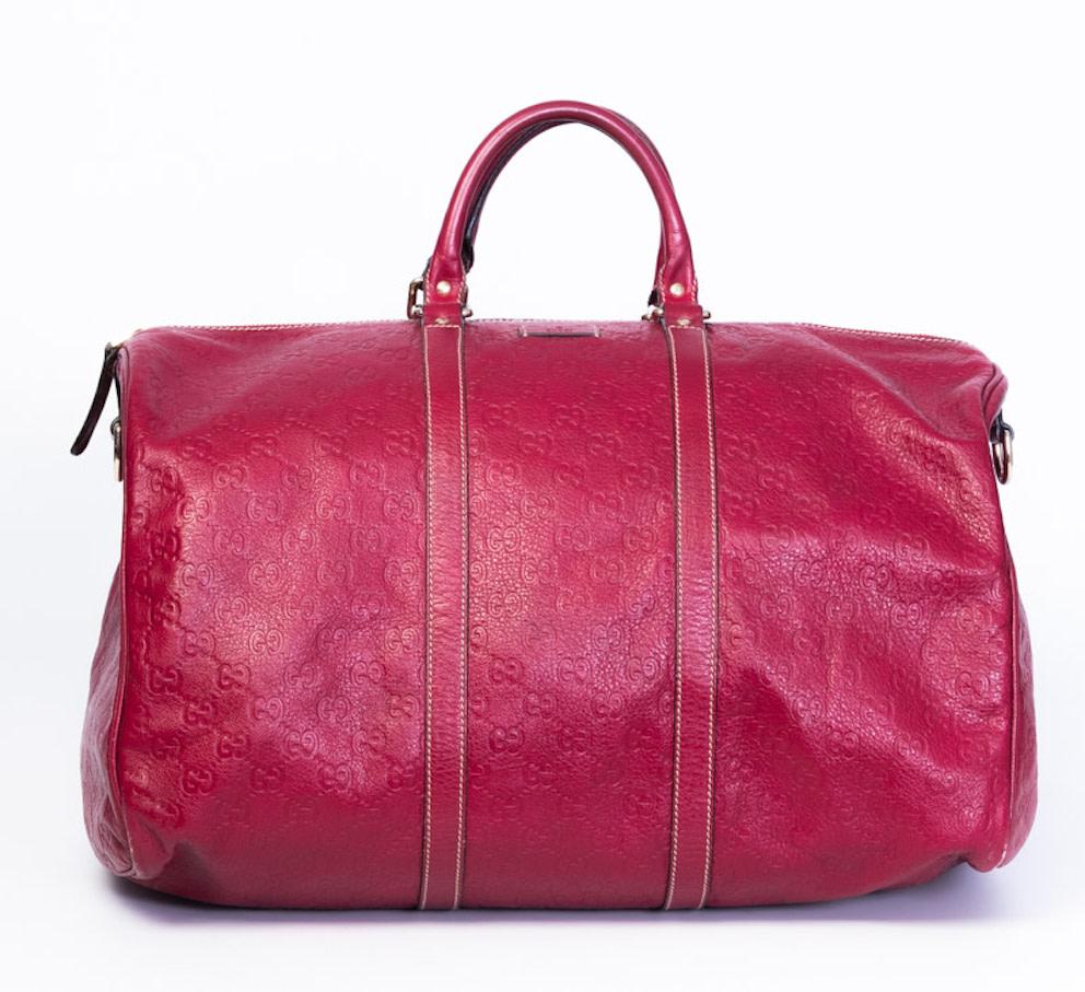 Ce sac de sport de style Boston est réalisé en cuir rouge embossé du monogramme GG de Gucci. Il est doté de poignées supérieures en cuir roulé et d'accessoires en laiton poli, d'une fermeture à glissière sur le dessus et d'une doublure intérieure en
