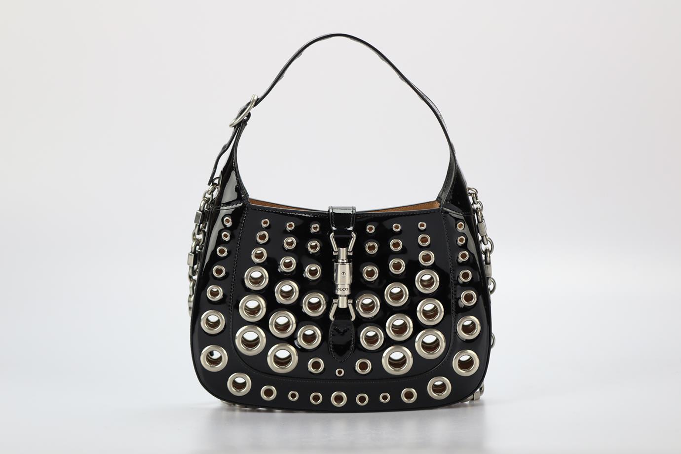 Gucci Ha Ha Ha Jackie 1961 Eyelet Embellished Patent Leather Shoulder Bag. Black. Clasp fastening - Front. Comes with - dustbag. Height: 13.8 in. Width: 11.1 in. Depth: 1.3 in. Handle drop: 6.6 in. Strap drop: 15 in. Condition: Used. Very good