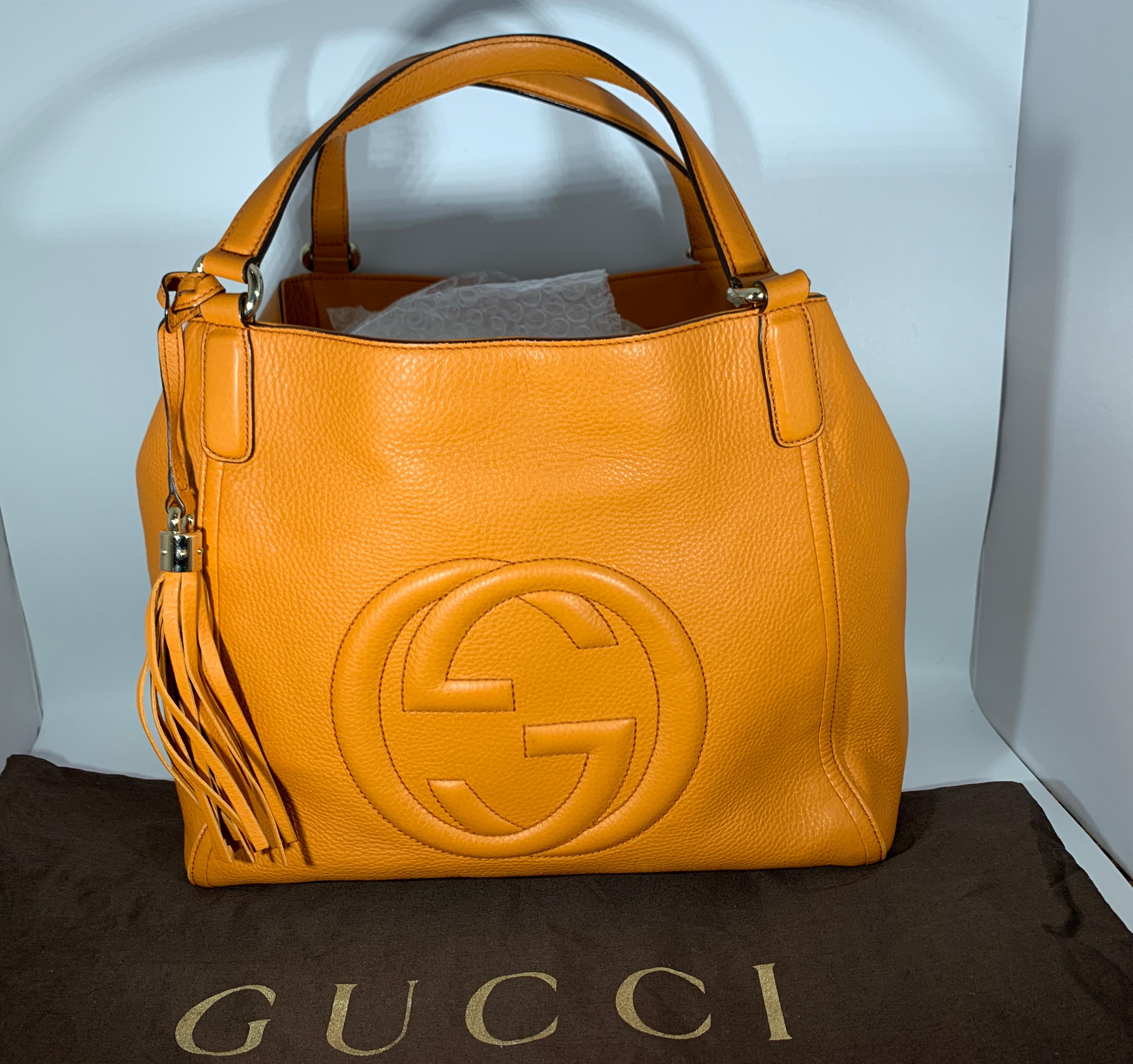 This chic tote is crafted of lovely fine grained calfskin leather in orange with an interlocking embossed GG logo. The bag features leather shoulder straps and a dangling leather tassel with a light gold cap. The top is open to a spacious natural