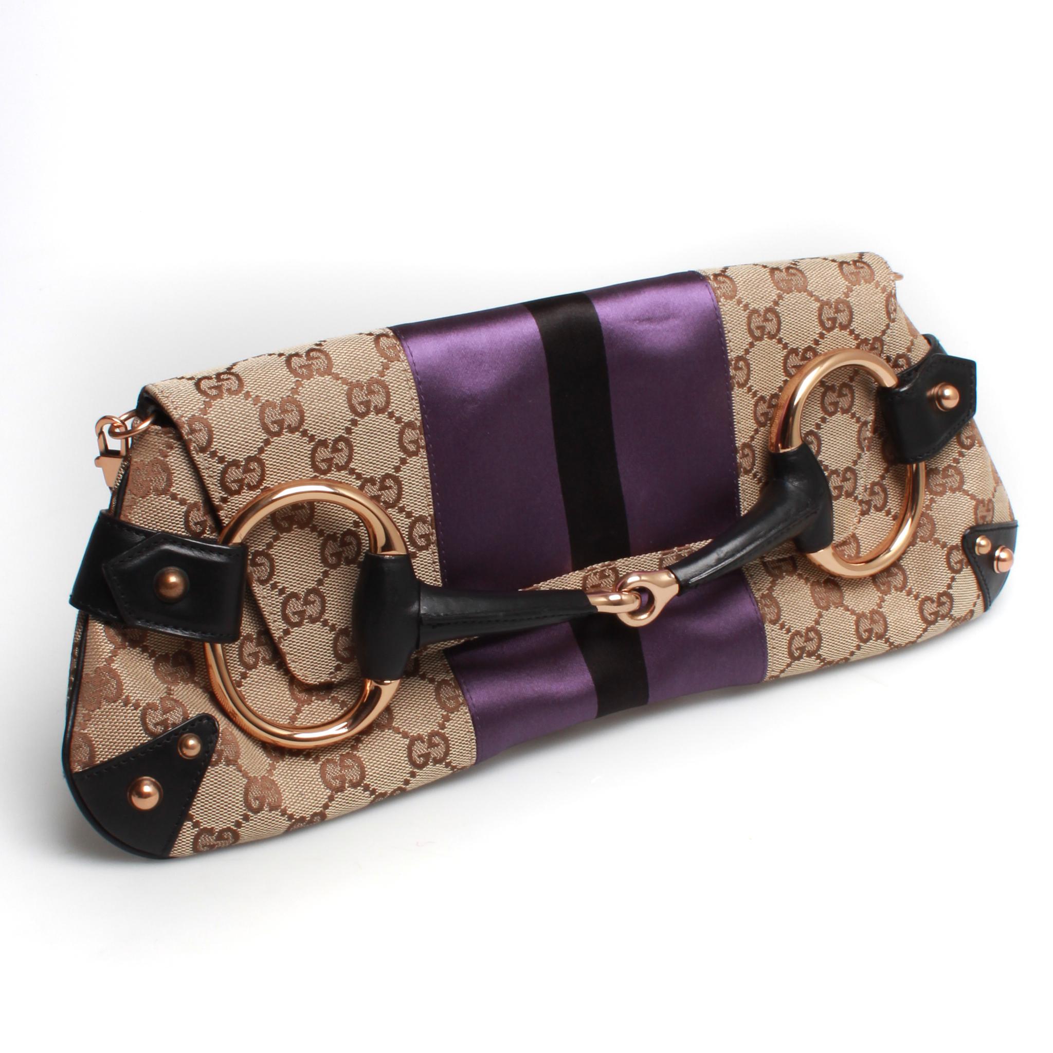 Gucci GG monogram canvas horsebit clutch. This incredible Tom Ford for Gucci era clutch bag features a silky satin purple and black central stripe, gold toned bronze shoulder or wrist strap with bamboo detailing, and large horse bit embellishment.
