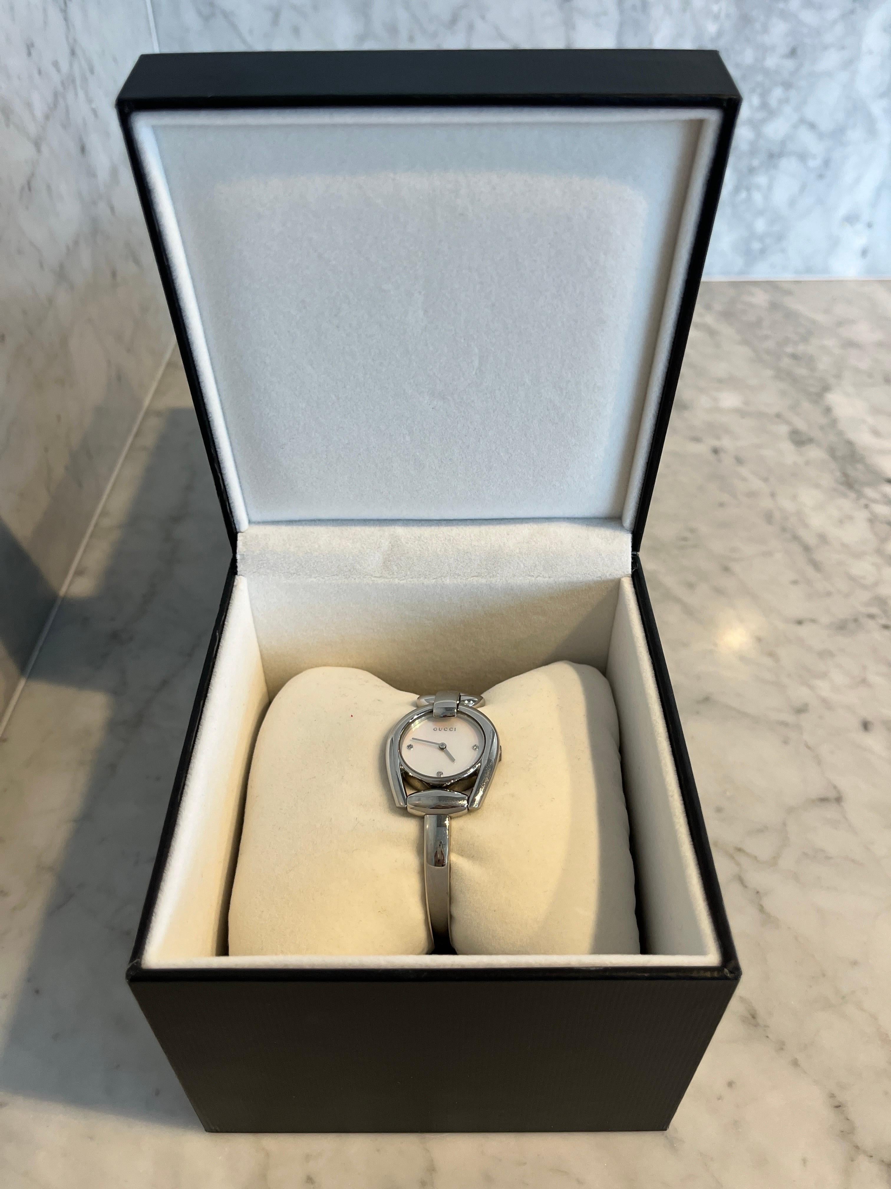 Montre Gucci classique avec robe ronde  en mors de cheval, avec cadran en nacre et trois index en cristal
Boîtier en acier inoxydable de 28 mm avec fenêtre de cadran en saphir antireflet
Mouvement à quartz suisse avec affichage analogique
Bracelet