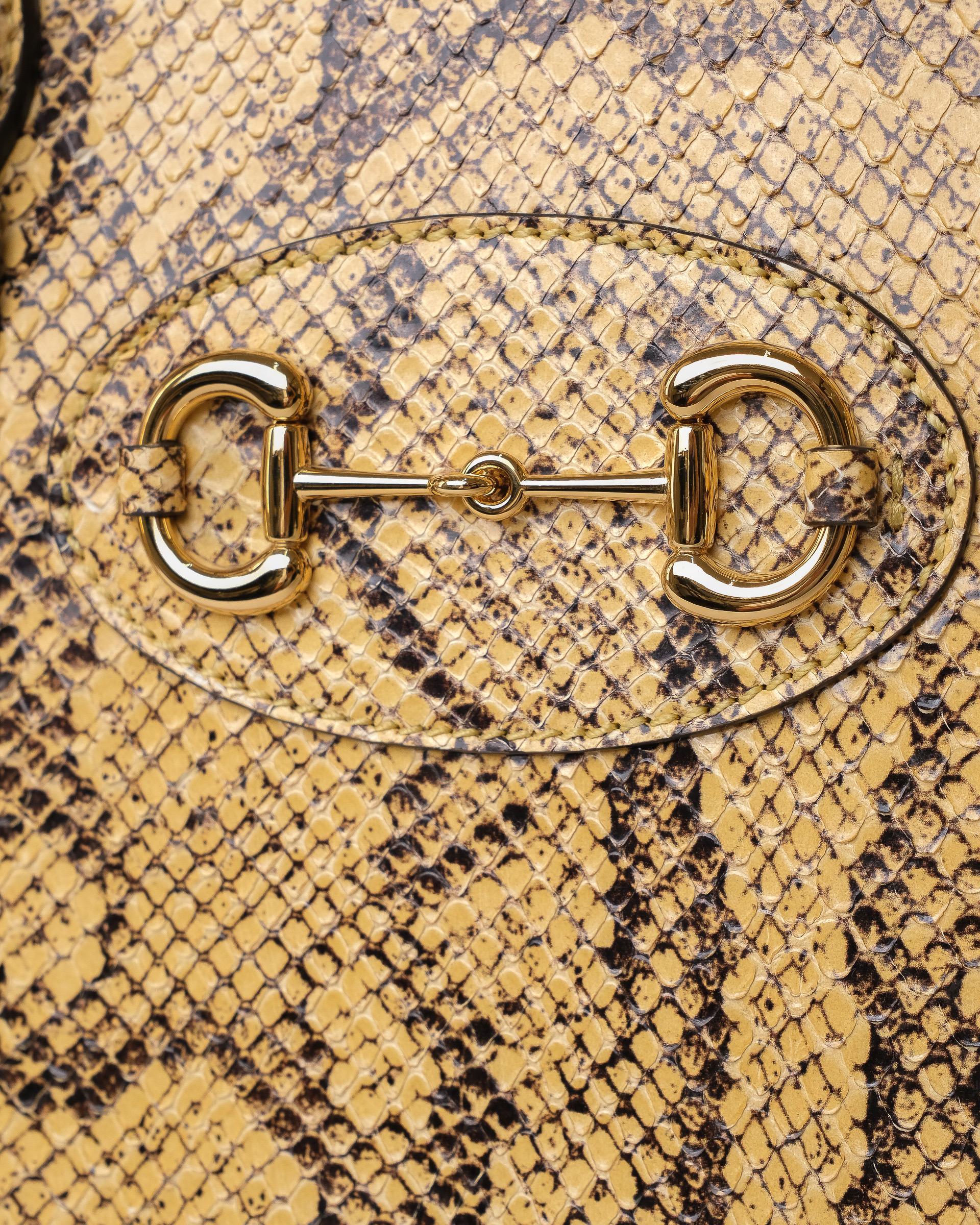 Borsa firmata Gucci, modello Horsebit Duffle, misura Medium, realizzata in pelle pitonata gialla con inserti in pelle nera e hardware neri. Dotata di una chiusura superiore a zip semicircolare, internamente rivestita in tela beige abbastanza