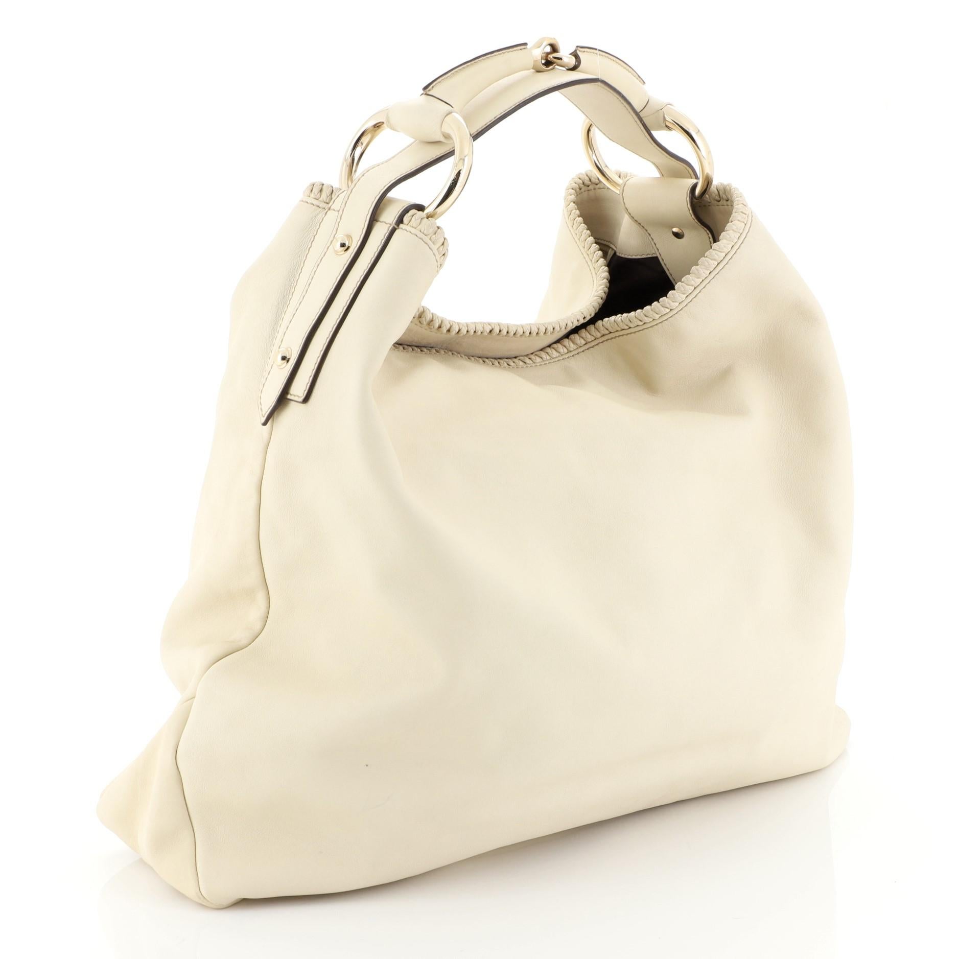This Gucci Horsebit Hobo Leather Large, crafted from neutral leather, features a single looped handle, gold-tone hardware, and metal horsebit accents. Its wide top opens to a brown fabric interior with zipped pocket. 

Estimated Retail Price: