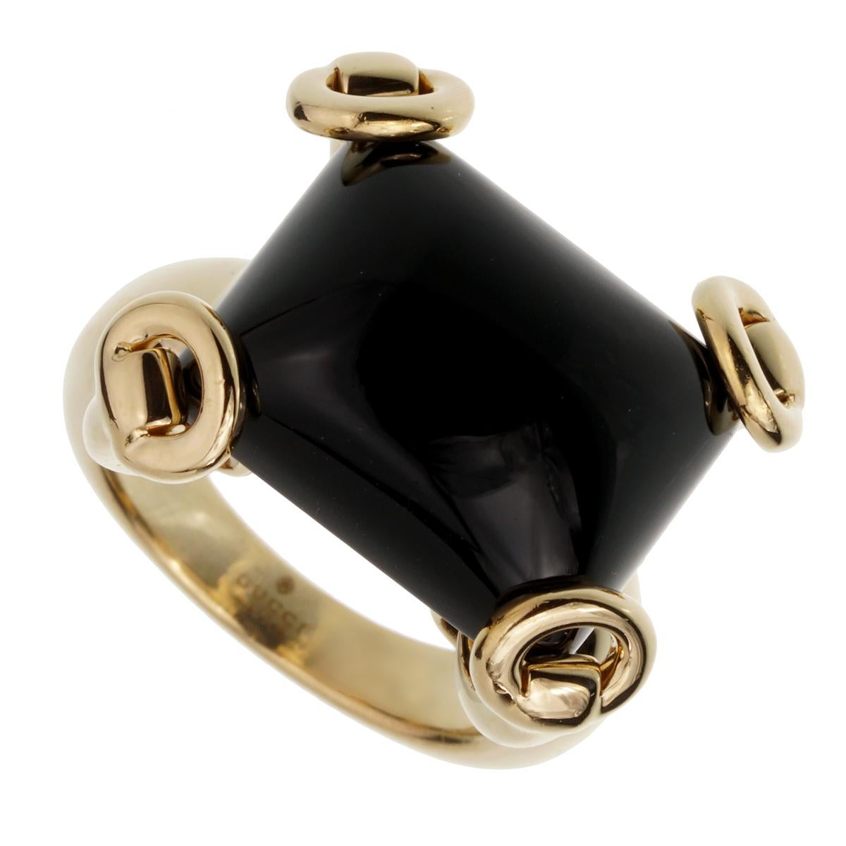 An iconic Gucci cocktail ring showcasing a cabochon Onyx set in 4 stirrup shaped motifs in shimmering 18k yellow gold. The ring measures measures a size 5 3/4 and can be resized.