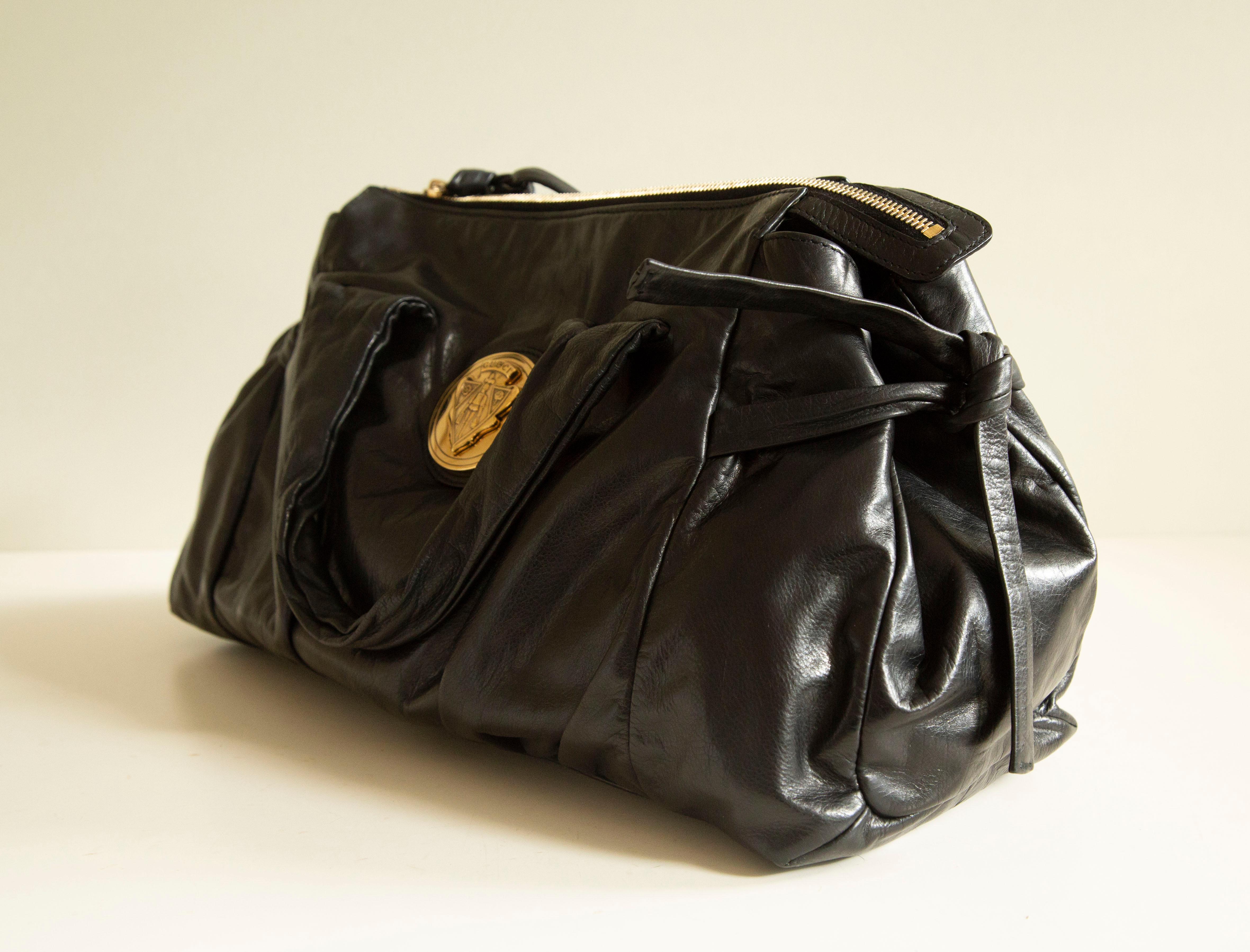 A Gucci Hysteria top handle bag made of soft and shiny black  leather with gold toned hardware. The interior is lined with the Gucci logo synthetic black  fabric. Next to the major compartment,  it features three side pockets of which one has a
