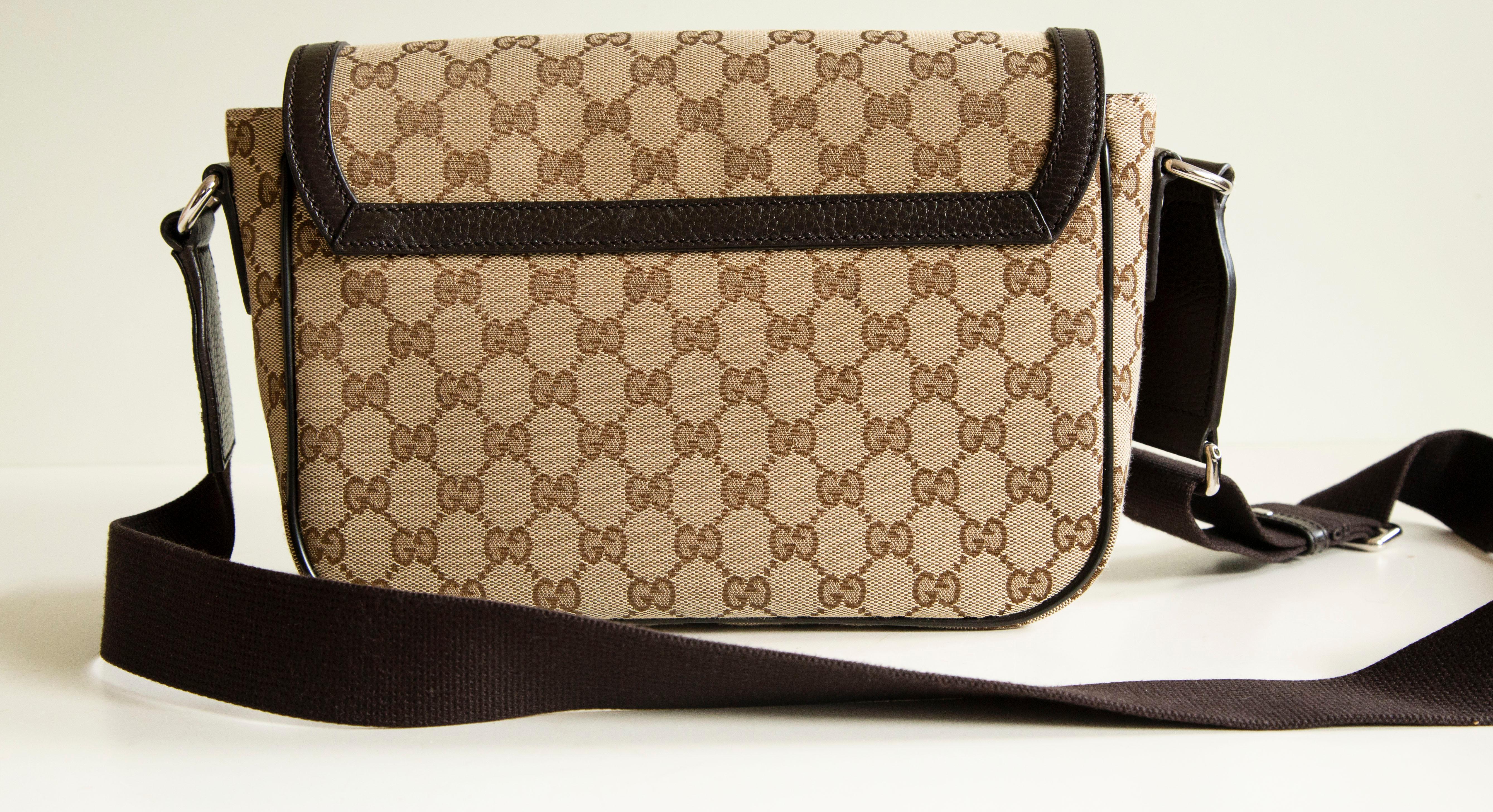 An unisex Gucci messenger bag in brown and beige canvas with brown leather trim. The bag features a GG web exterior, brown leather trim, and silver-tone hardware. The interior is lined with brown fabric and there are three side pockets of which one
