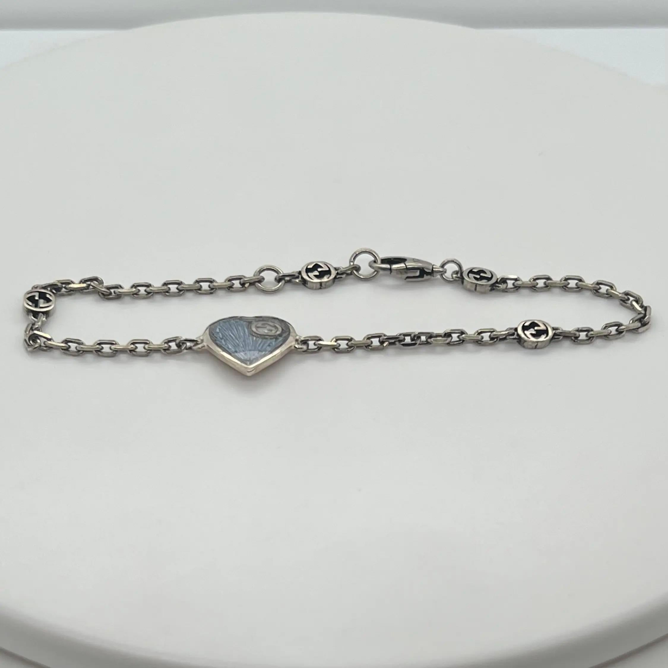 This trendy GUCCI bracelet is designed in 925 sterling silver. It features an intricately engraved light blue heart pendant with an interlocking G symbol attached to a woven link chain. Giving the classic motif a bright and playful twist is light