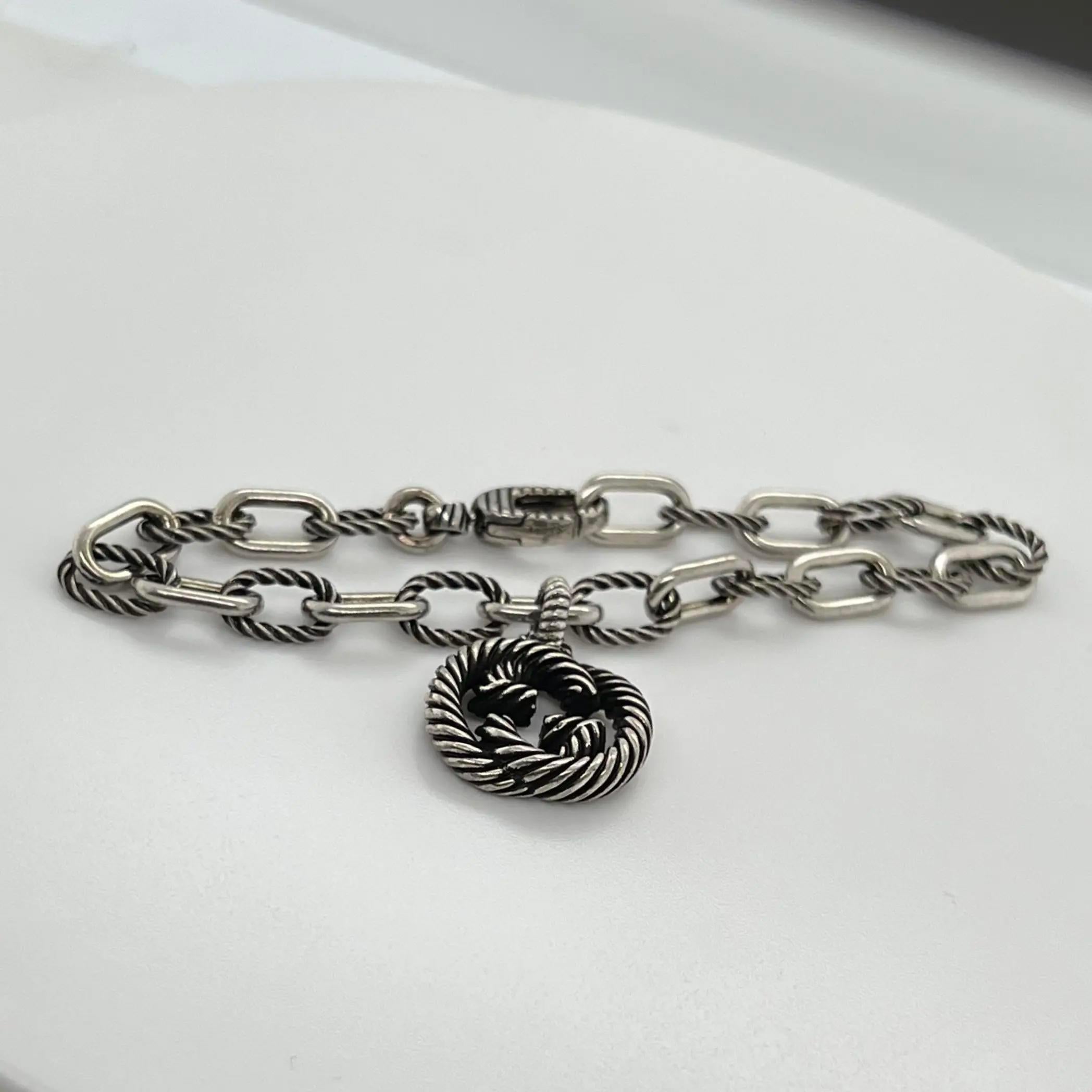 This GUCCI bracelet features an interlocking G twisted charm hanging at the center with an aged finished twisted link chain. Designed in 925 Sterling Silver. Bracelet length: 7 Inches. Total weight: 14.81 grams. Made in Italy. Unworn condition. The
