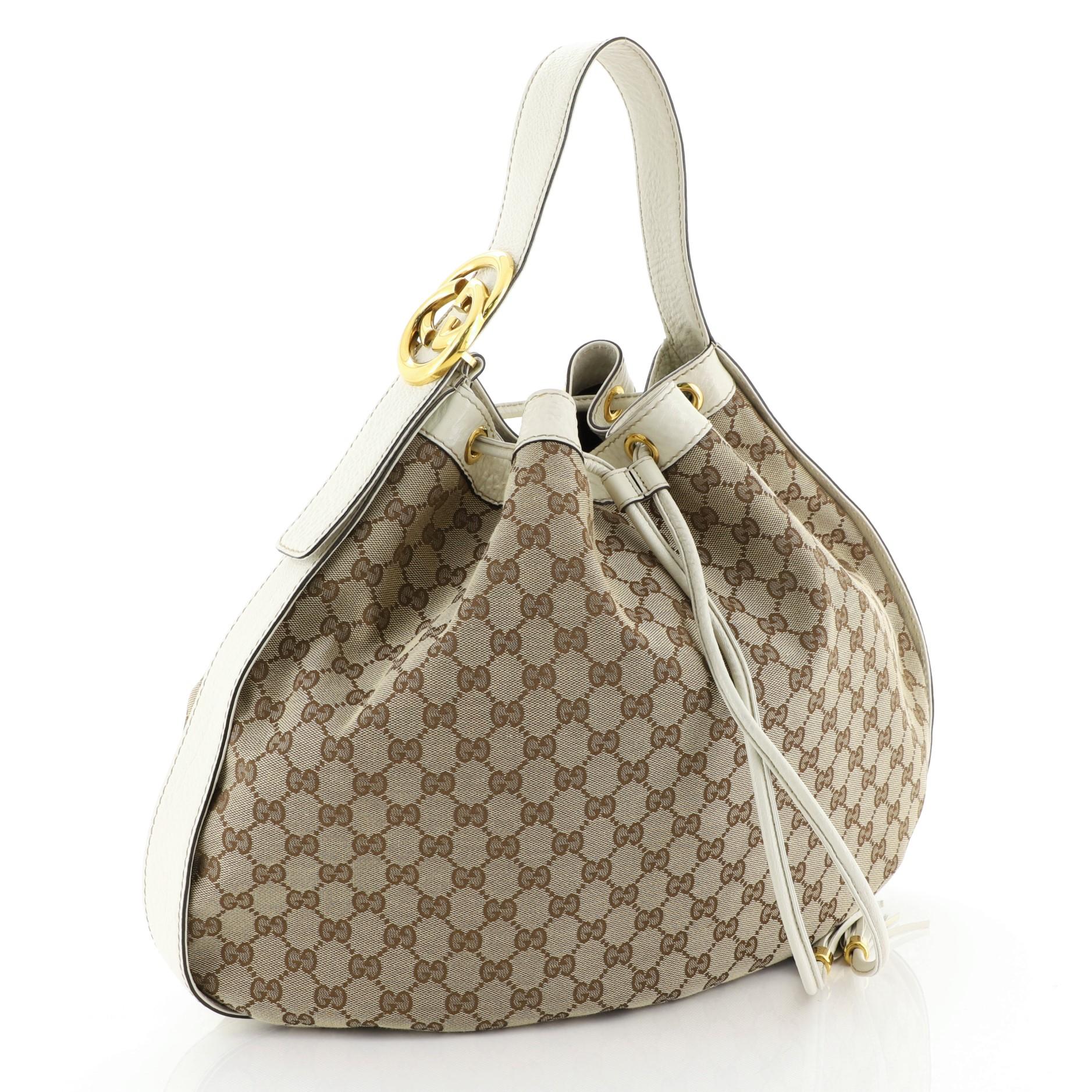 This Gucci Interlocking Icon Drawstring Hobo GG Canvas Large, crafted in brown GG monogram canvas, features a flat adjustable shoulder strap, leather trim, drawstring with tassel details, and gold-tone hardware. Its drawstring closure opens to a