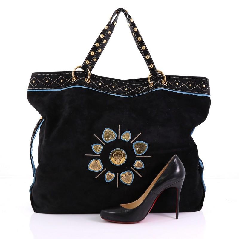 This Gucci Irina Babouska Tote Suede, crafted from black suede, features dual flat handles with studs, Gucci medallion embellishments at its front center with engraved crested hearts, studded top trims, and gold-tone hardware. Its magnetic snap