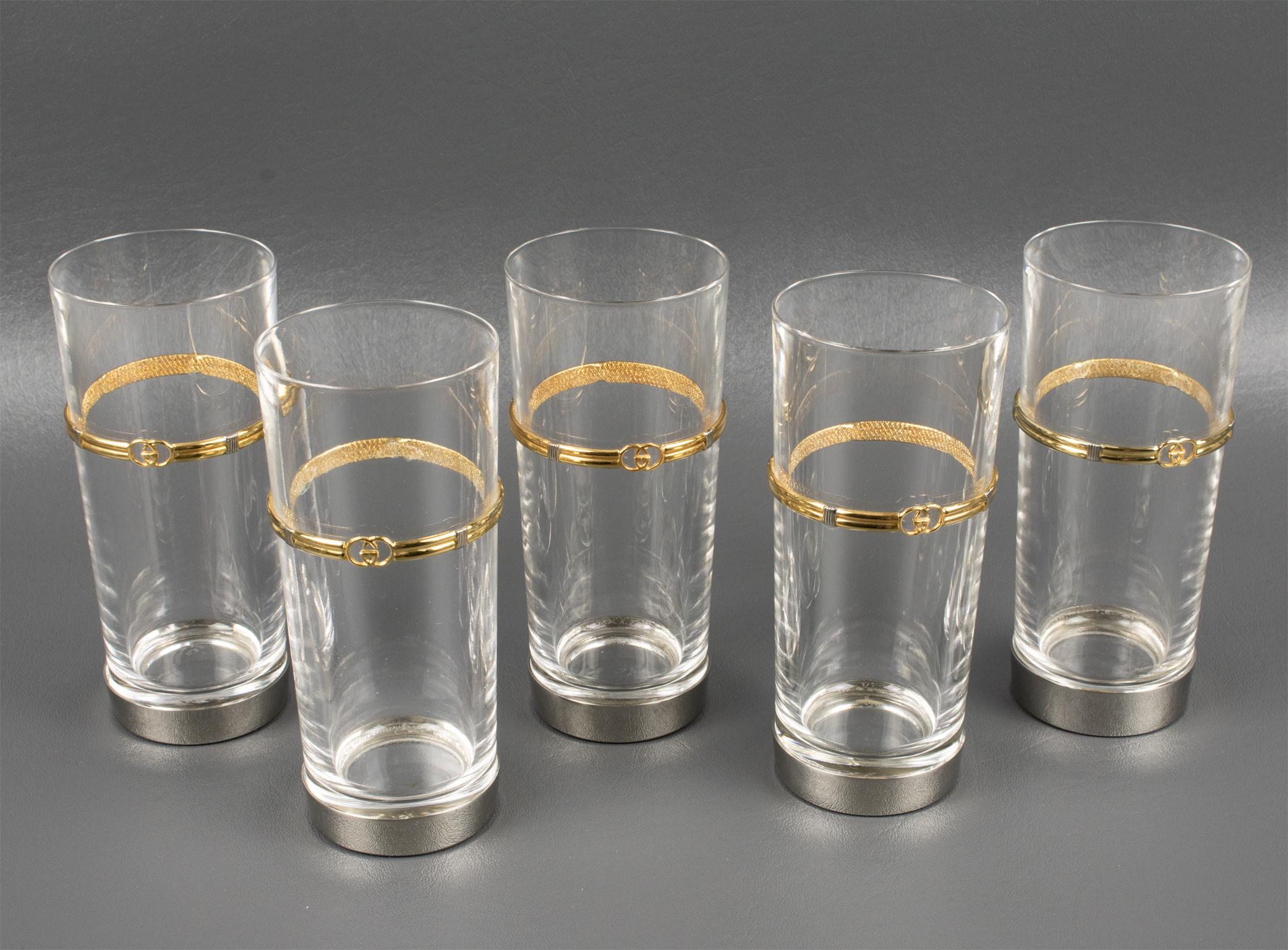 Entertain with style with this Gucci barware set of crystal highball tumbler glasses with a gold-plated GG logo.
This chic Italian hallmarked Gucci set of five glasses features tall tumbler-shaped crystal glasses with silver-plated metal bases and