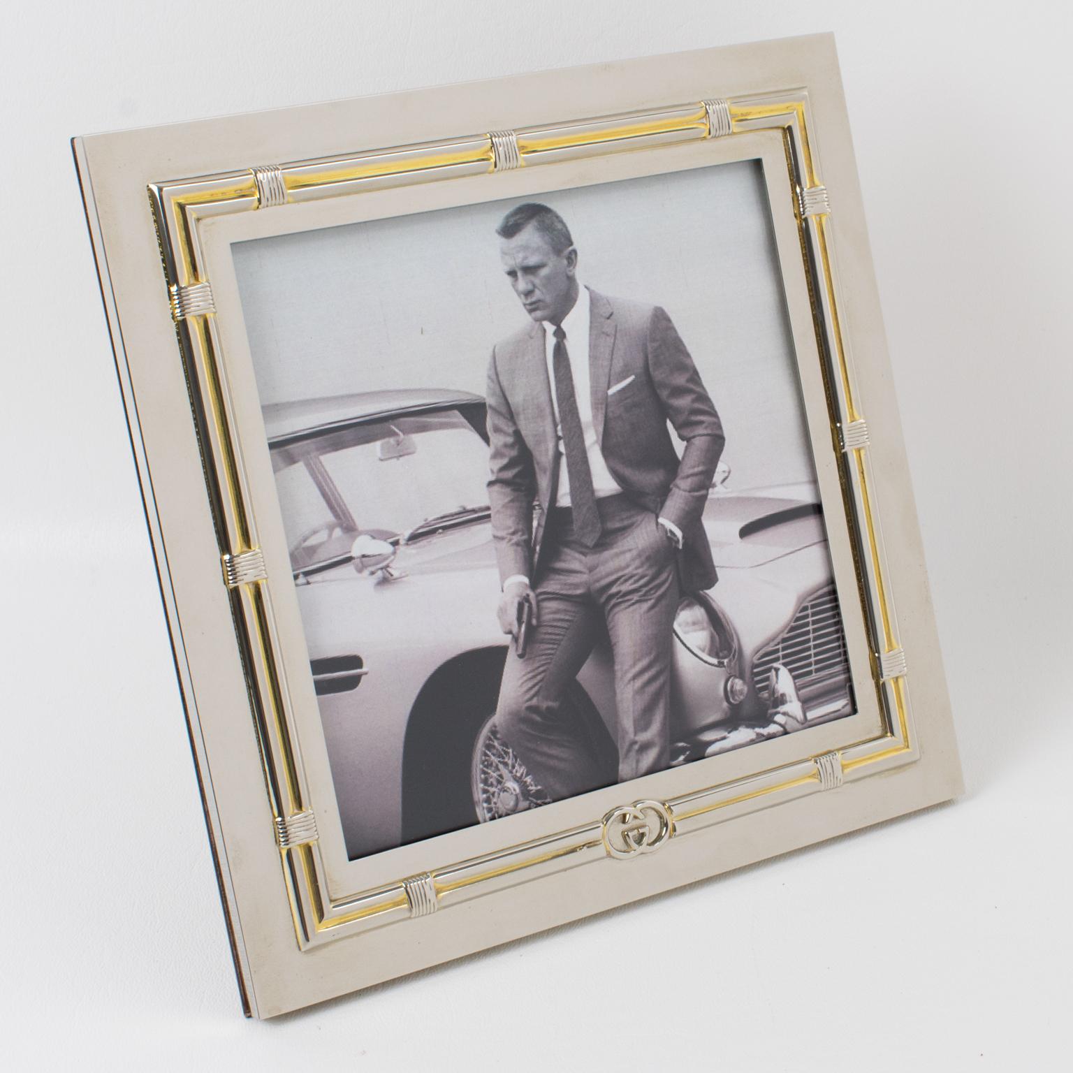 So elegant picture photo frame by Italian designer Gucci. Square shape in silver plate with gold plate accents in the carved design all around. GG logo on the front and also at the back. High gloss wood back and easel. Stamped 