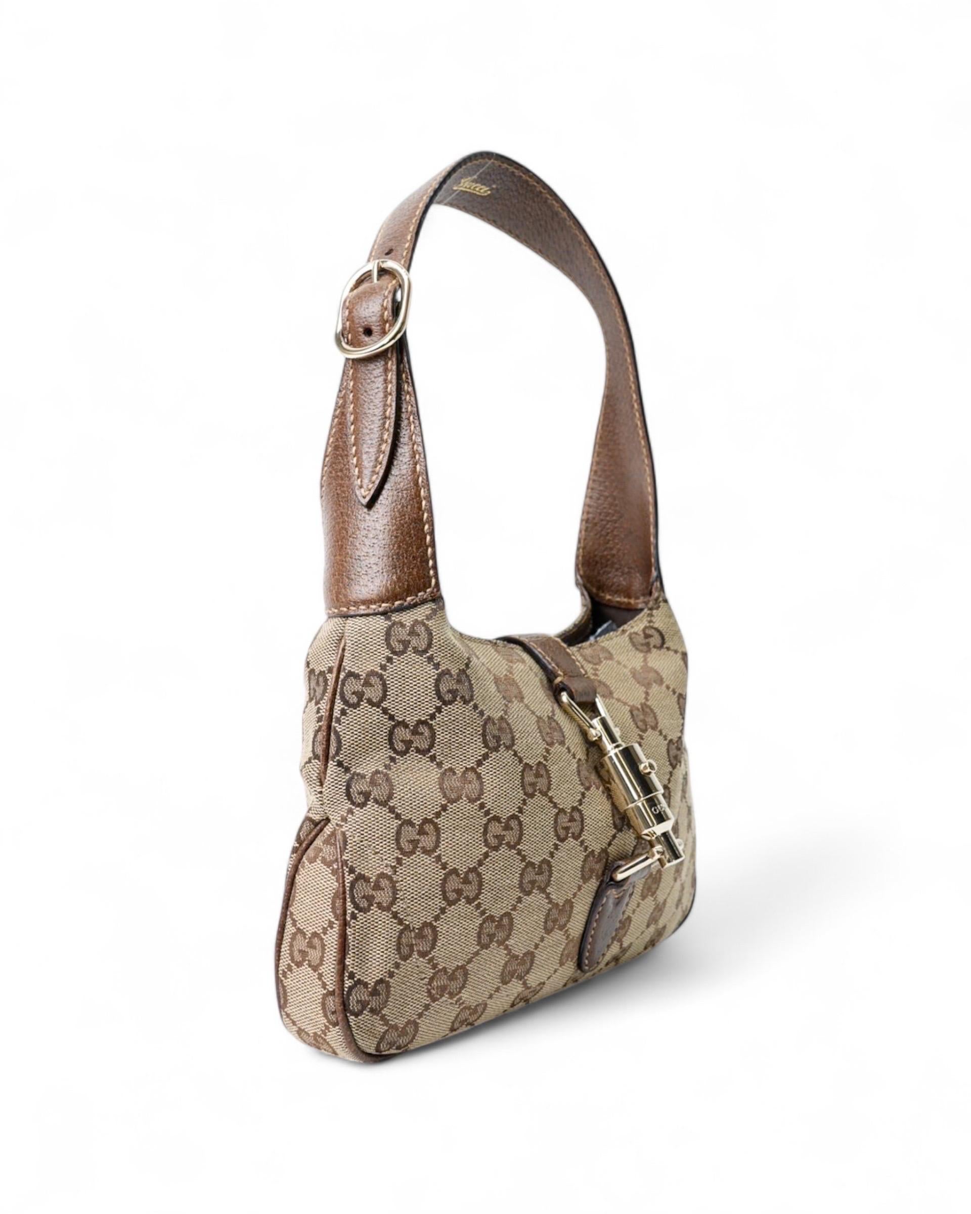 Borsa firmata Gucci, modello Jackie Mini, realizzata in tela beige nella classica fantasia GG Supreme con inserti in pelle e hardware dorati. Dotata di una chiusura ad incastro, internamente rivestita in tela marrone e comoda tasca con zip. Munita