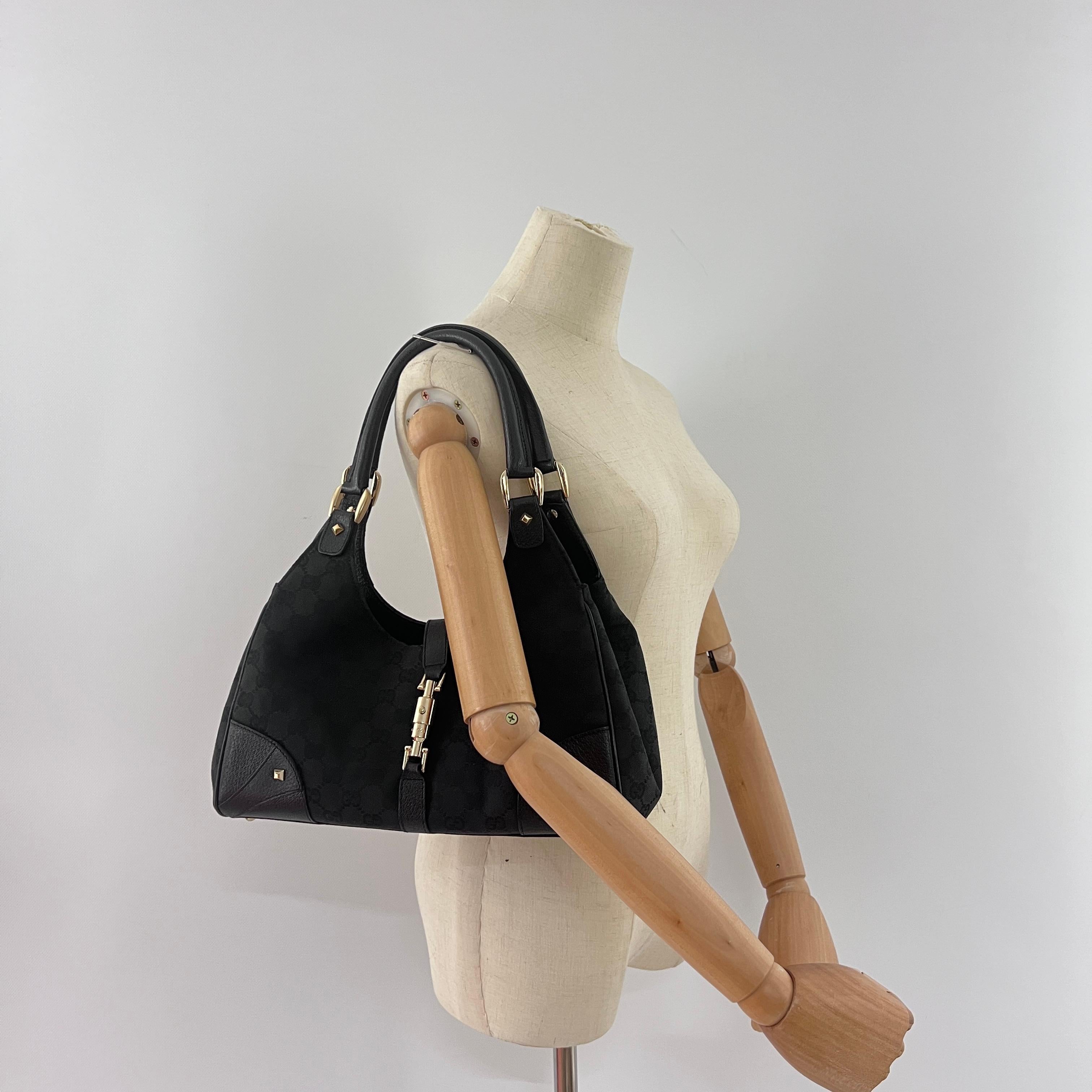 Borsa a tracolla Jackie di Gucci in tela e pelle nera con finiture in argento. La borsa ha una chiusura a scatto. L'interno è composto da uno scomparto principale. Può essere indossato sulla spalla. La borsa è in ottime condizioni, leggermente