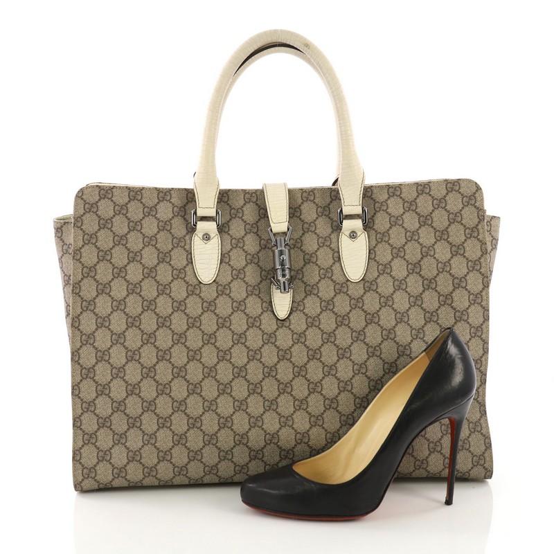 This Gucci Jackie Soft Tote GG Coated Canvas Large, crafted in brown GG coated canvas, features dual rolled leather handles and gunmetal-tone hardware. Its piston-lock closure opens to a brown canvas interior. **Note: Shoe photographed is used as a