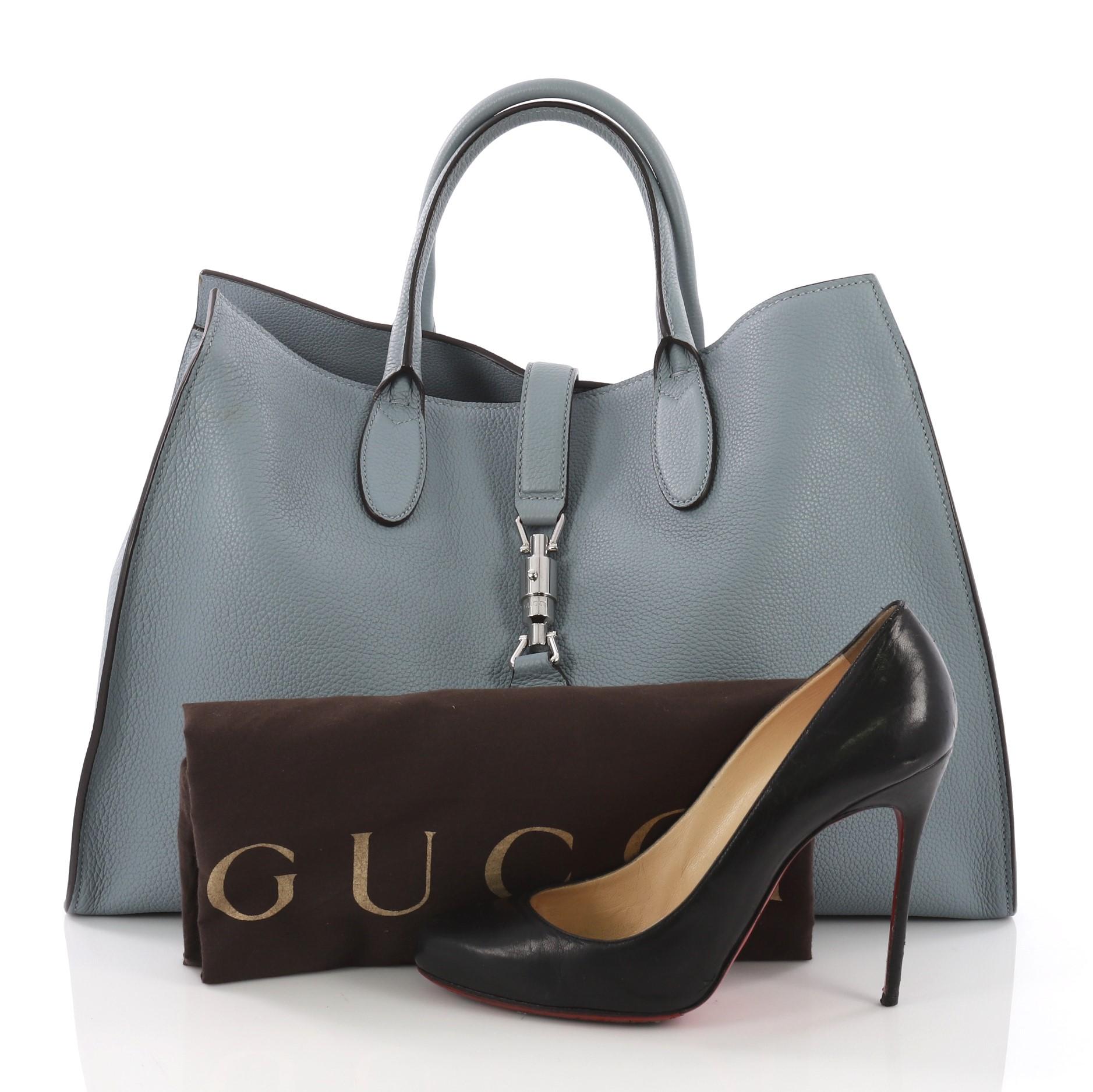 This Gucci Jackie Soft Tote Leather Large, crafted from blue soft leather, features a soft-structured silhouette, dual rolled handles, and silver-tone hardware. Its piston-lock closure opens to a blue raw leather interior with side zip pockets.
