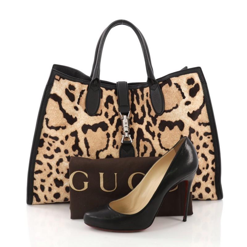 This Gucci Jackie Soft Tote Printed Calf Hair Large, crafted in brown Printed Calf Hair, features dual rolled leather handles, black leather trim, and silver-tone hardware. Its piston-lock closure opens to a beige suede interior with zip pockets.