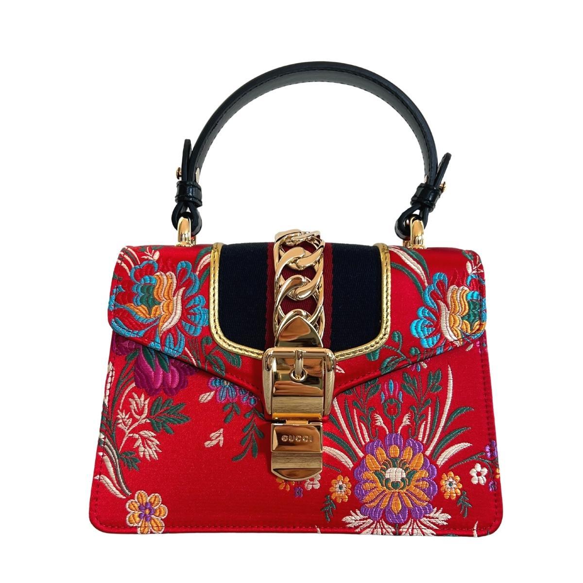 Red brocade Sylvie bag is crafted to a compact, structured shape with black leather trims, and detailed with all the house hallmarks: navy and red Web stripe, gold-tone metal chain, and logo-engraved buckle-effect clasp.
One leather top
