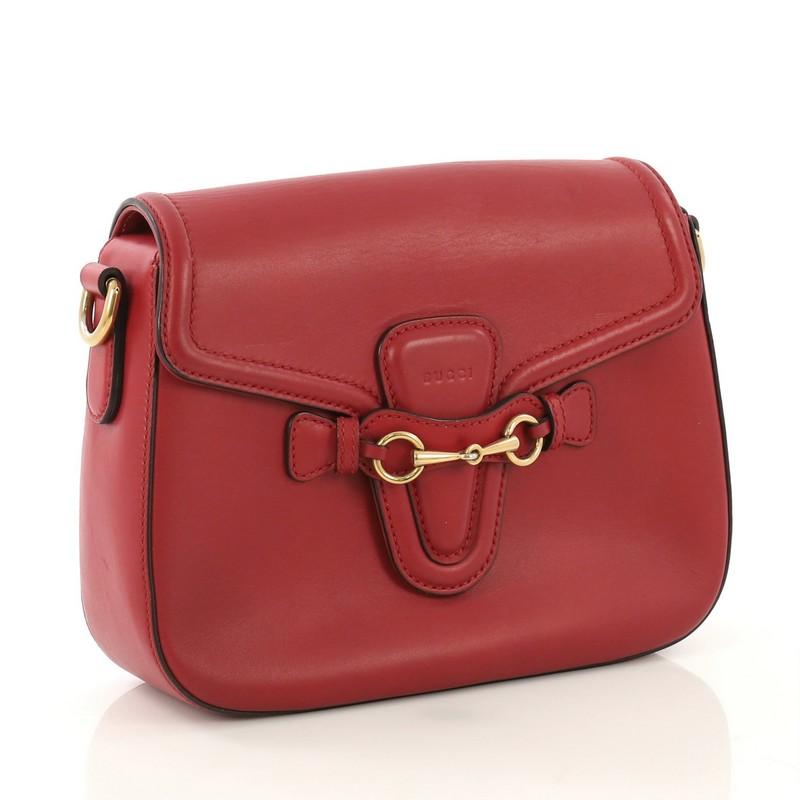 This Gucci Lady Web Shoulder Bag Leather Medium, crafted from red leather, features a detachable shoulder strap, embossed Gucci logo, and aged gold-tone hardware. Its flap closure with horsebit buckle detail opens to a beige fabric interior with