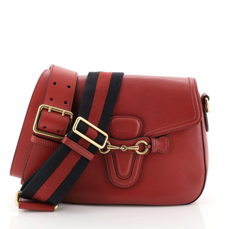 This Gucci Lady Web Shoulder Bag Leather Medium, crafted from red leather features a detachable signature web nylon shoulder strap, hand-painted edges, embossed Gucci logo and aged gold-tone hardware. Its flap closure with horsebit buckle detail