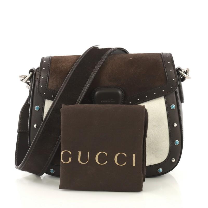 This Gucci Lady Web Shoulder Bag Printed Pony Hair with Studded Leather Medium, crafted from brown printed pony hair with leather trim, features hand-painted edges, and silver-tone hardware. Its flap closure with horsebit buckle detail opens to a