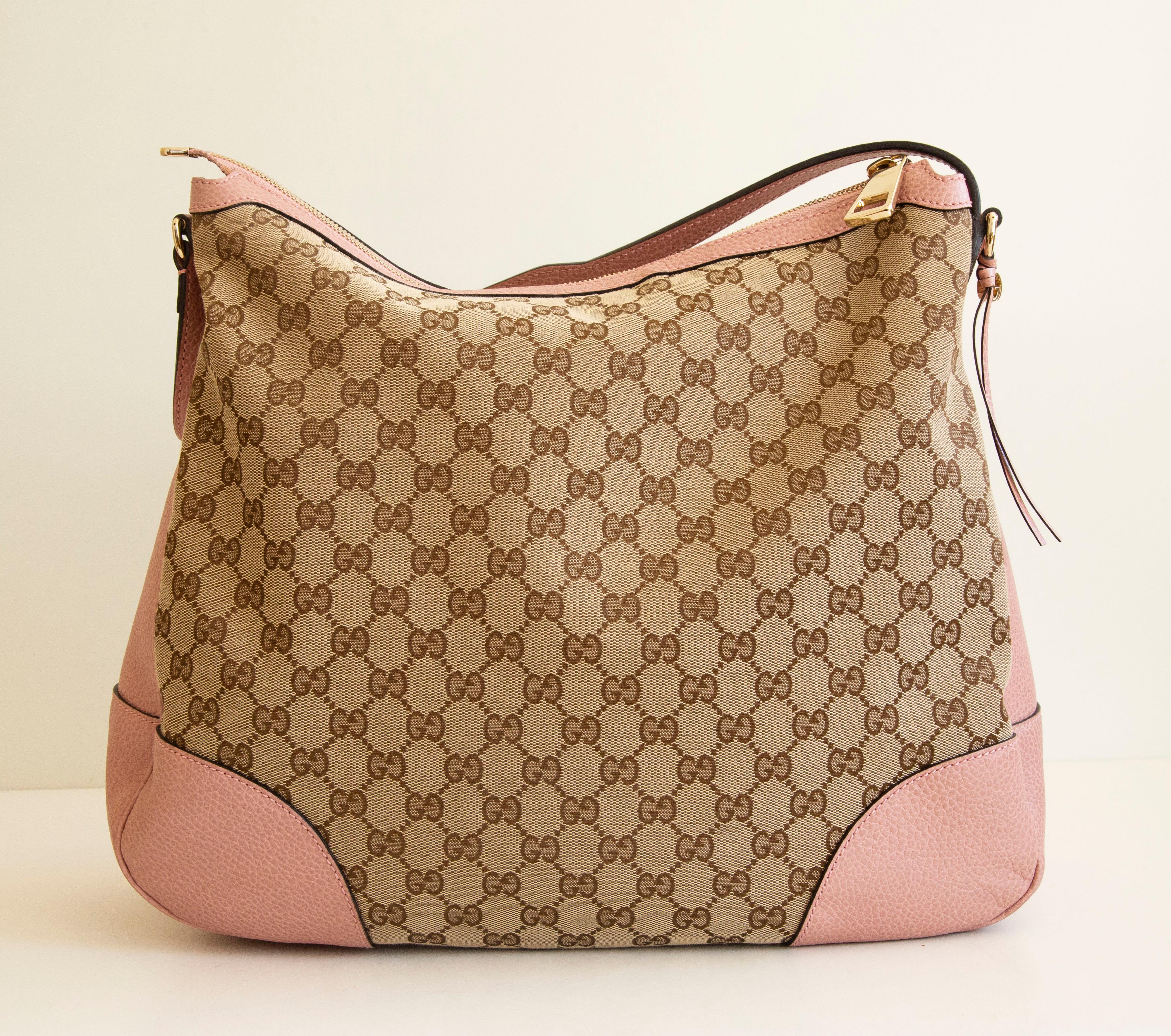 An authentic Gucci Bree shoulder bag/hobo bag. The bag features a GG canvas exterior, pink leather trim, and light-gold-toned hardware. The interior is lined with beige fabric and there are three side pockets, one zipped pocket, and two slip